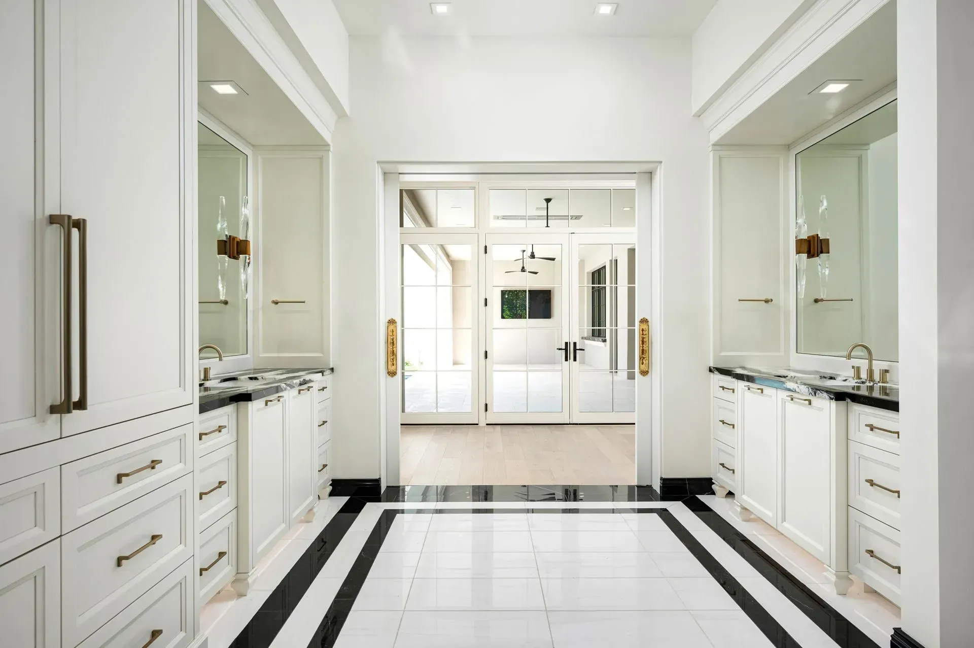 White bathroom with black and white floor, dual sinks, mirrors, and glass doors.