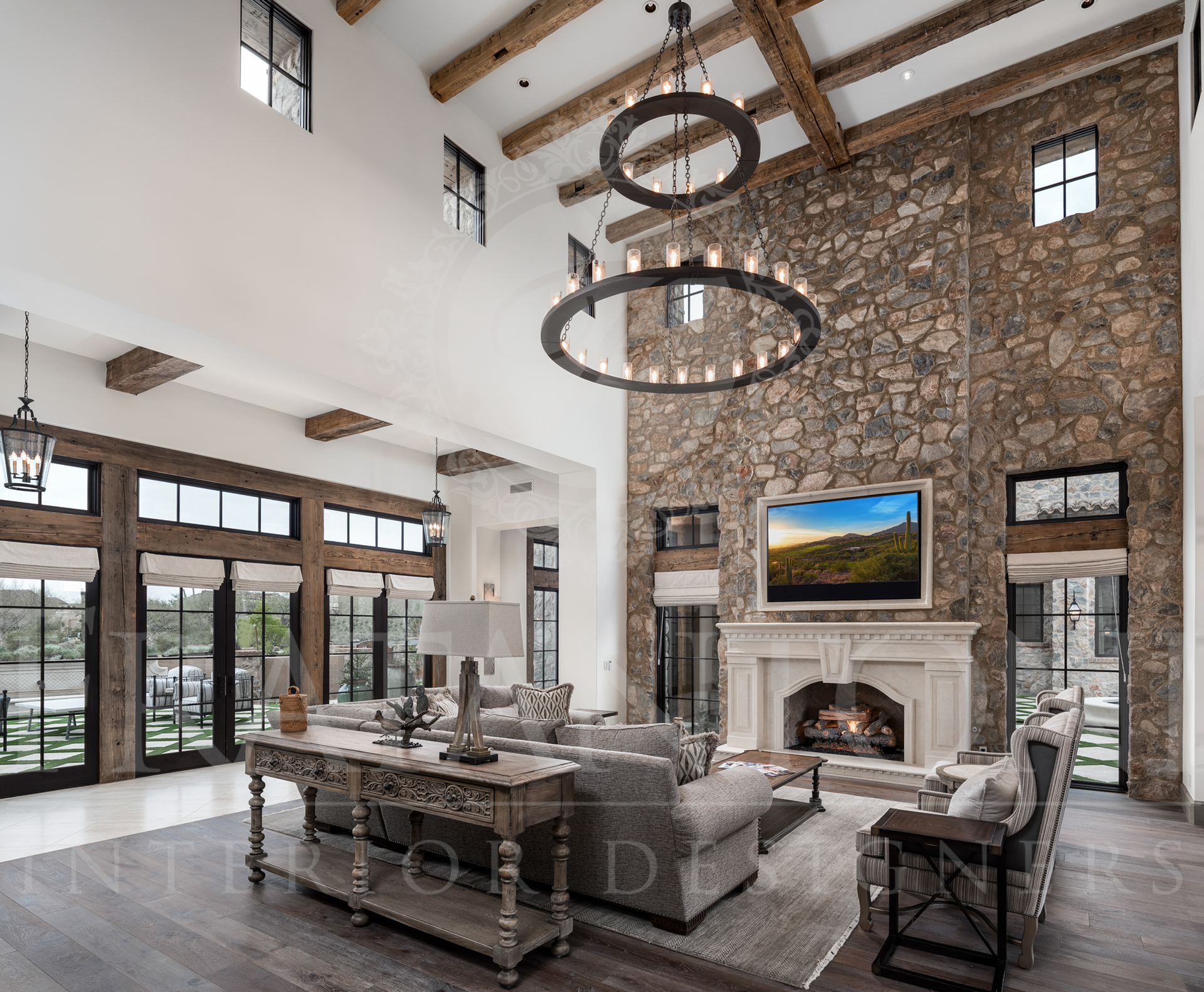 Spacious living area with stone wall, marble fireplace, large windows, and decorative chandelier.