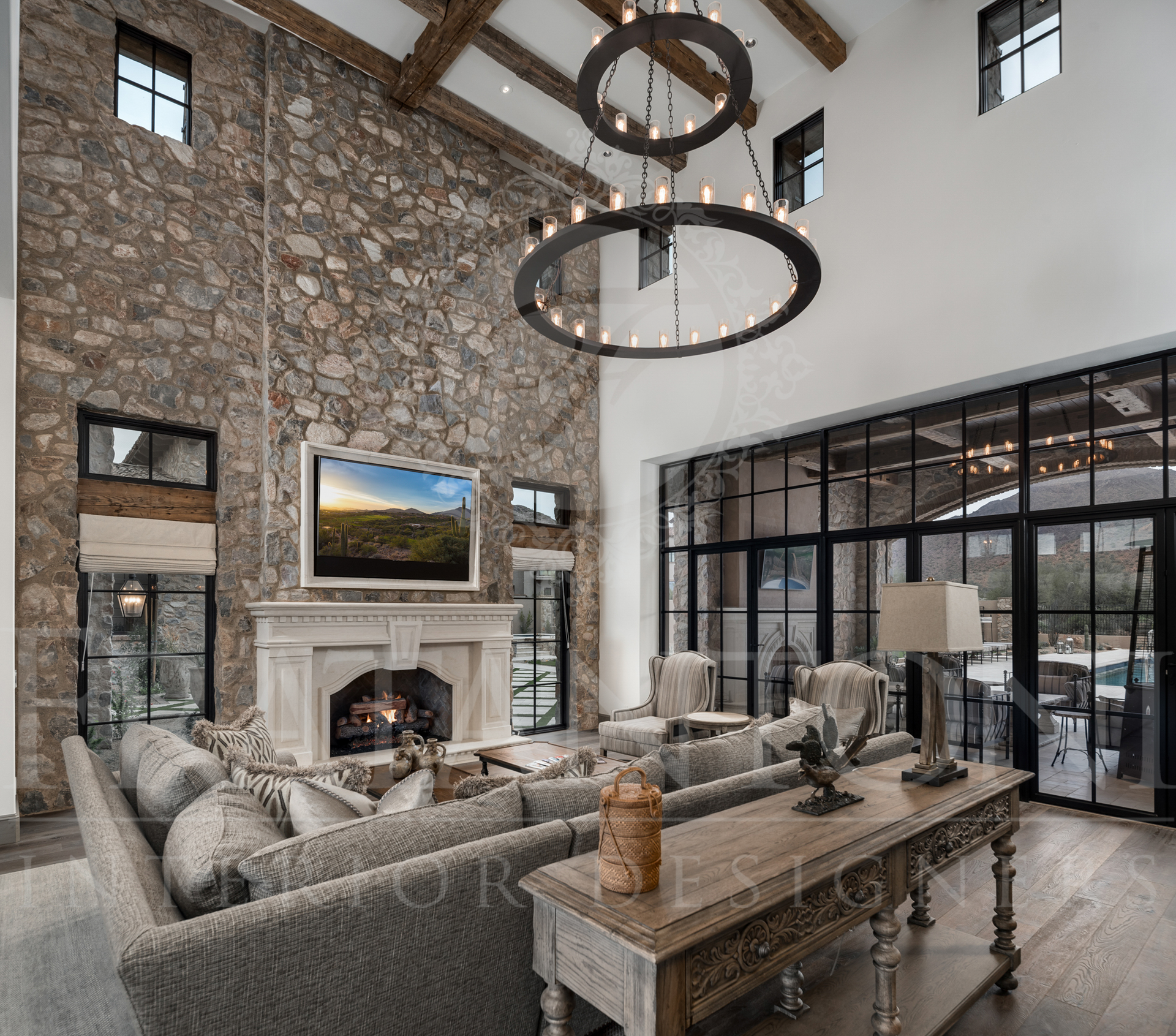 Luxurious living room with stone wall, fireplace, large glass doors with patio access, and chandelier all designed by fratantoni interior designers in scottsdale arizona. 