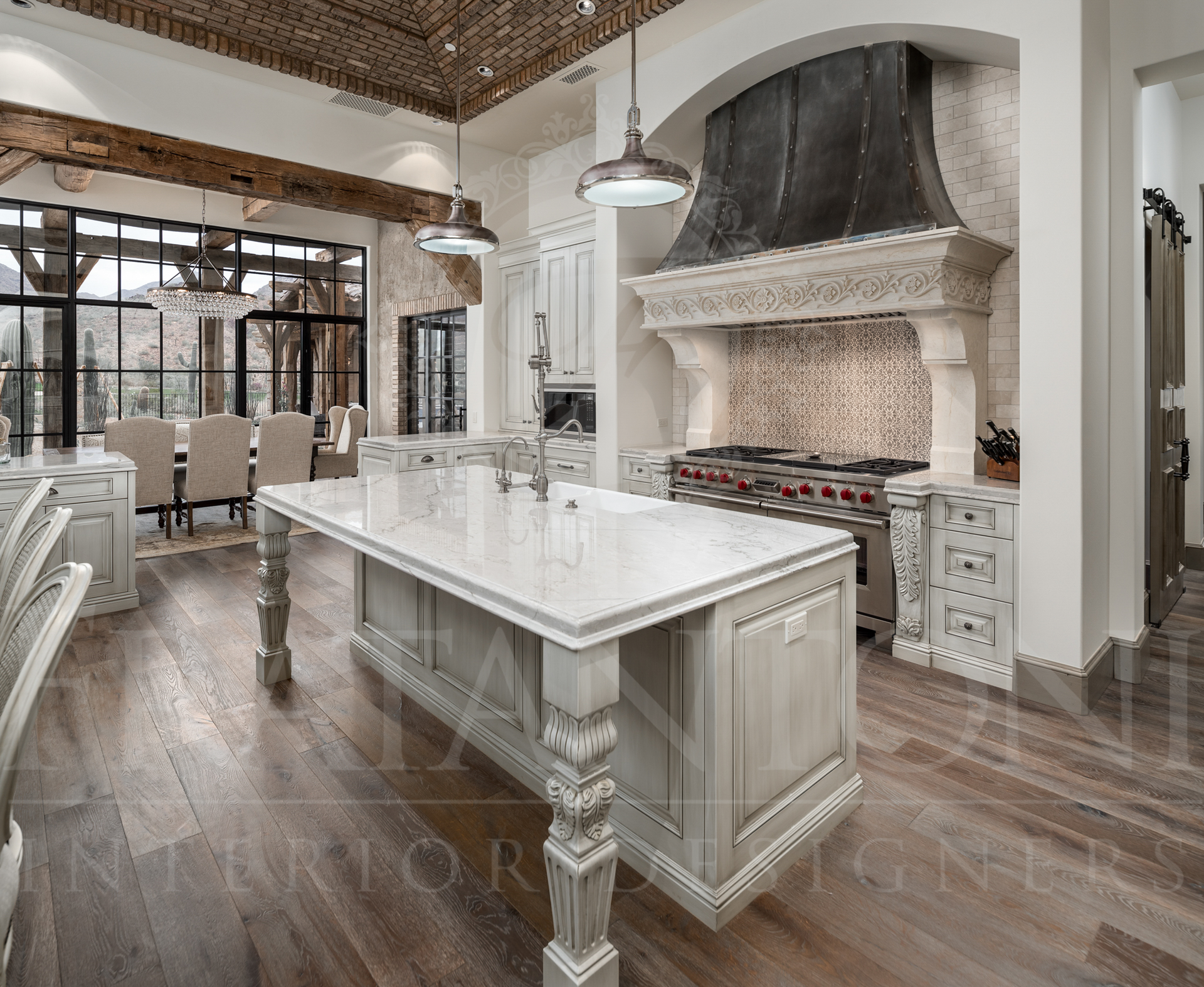 Elegant kitchen with large island, stove with custom ornate hood, and wood floors.