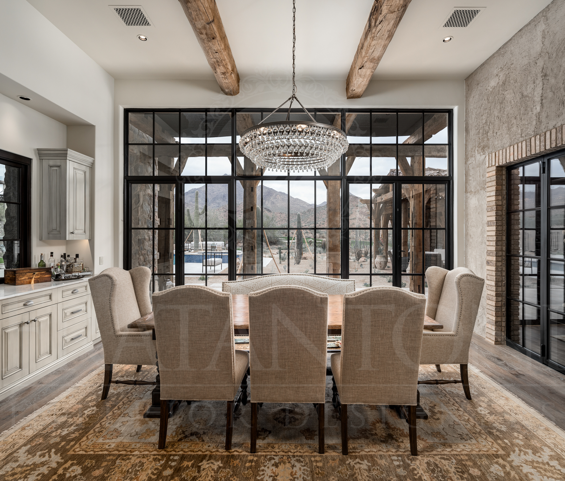 Dining room with large window overlooking desert mountains, dining table, chandelier, exposed beams, and chairs designed by luxury interior designers in Scottsdale, arizona. 