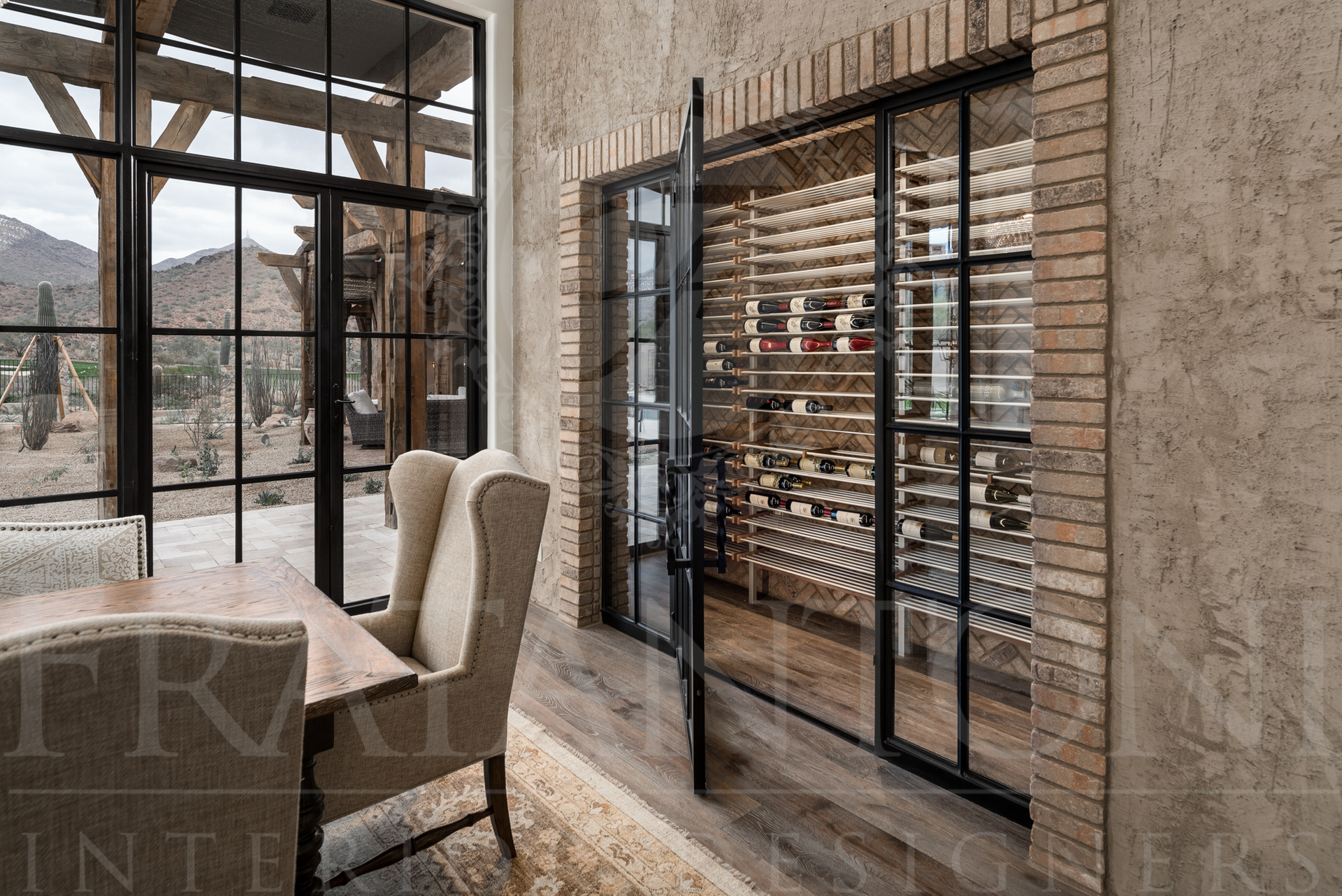 A wine cellar with a glass and metal door, table, and outdoor view through a large window.