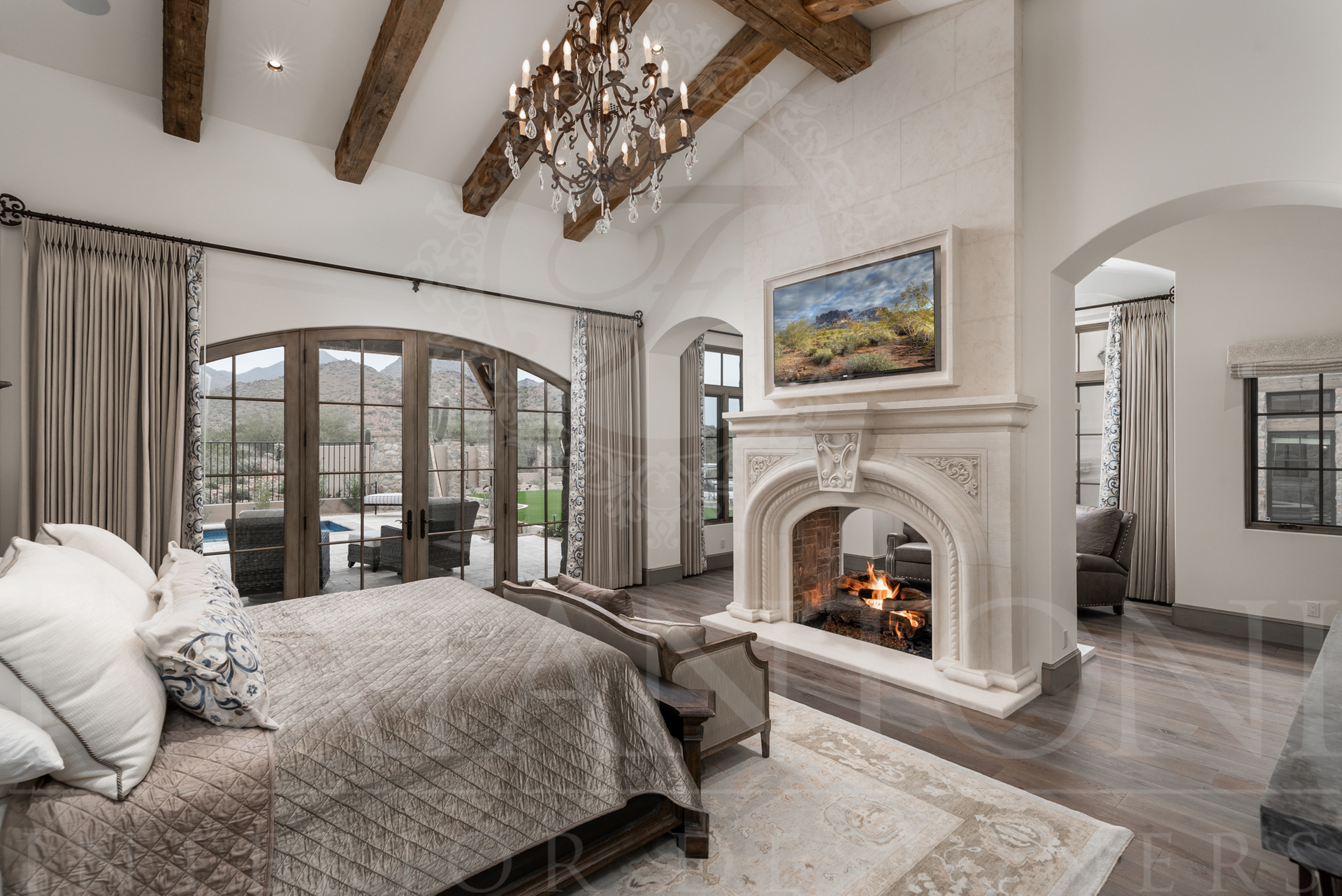 Luxurious master bedroom with two-sided stone fireplace, arched doors, and decorative beams designed by Fratantoni Interior Designers