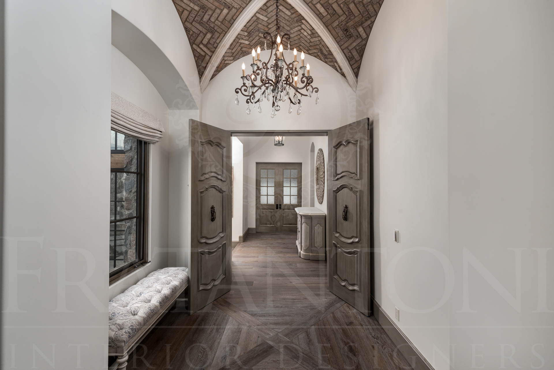 Long hallway with arched brick ceiling, large wooden doors, chandelier, bench, and window.