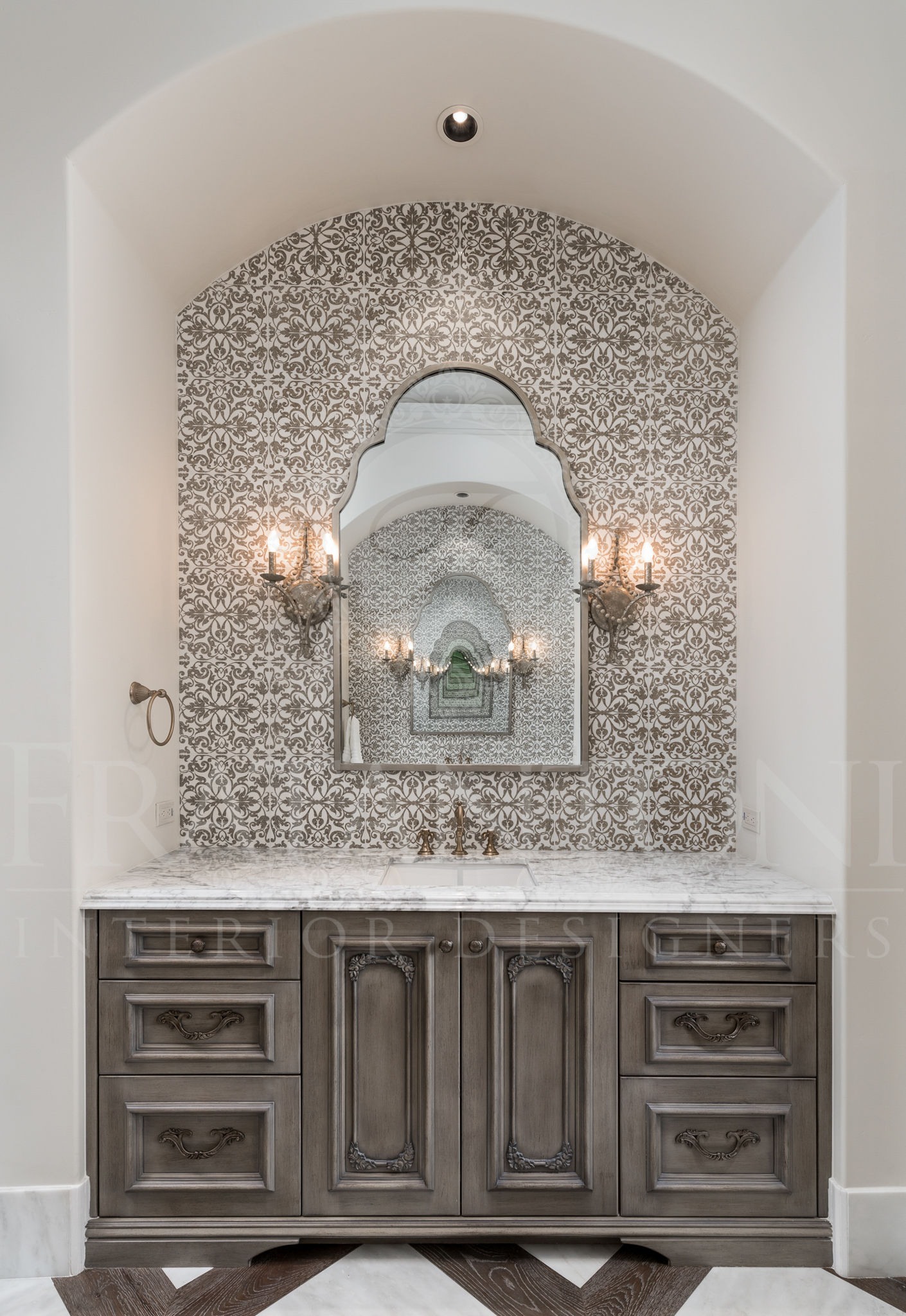 Neutral bathroom vanity with arched mirror, mosaic tile backsplash, gray cabinets, sconces.