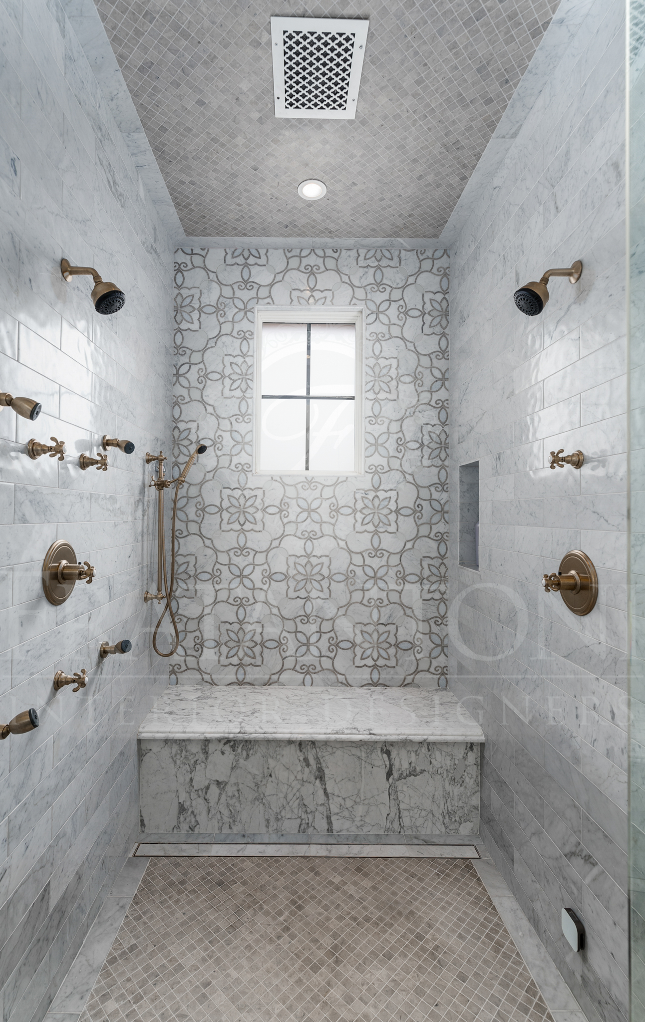 Luxurious tiled shower with multiple brass showerheads, built-in bench, and window.