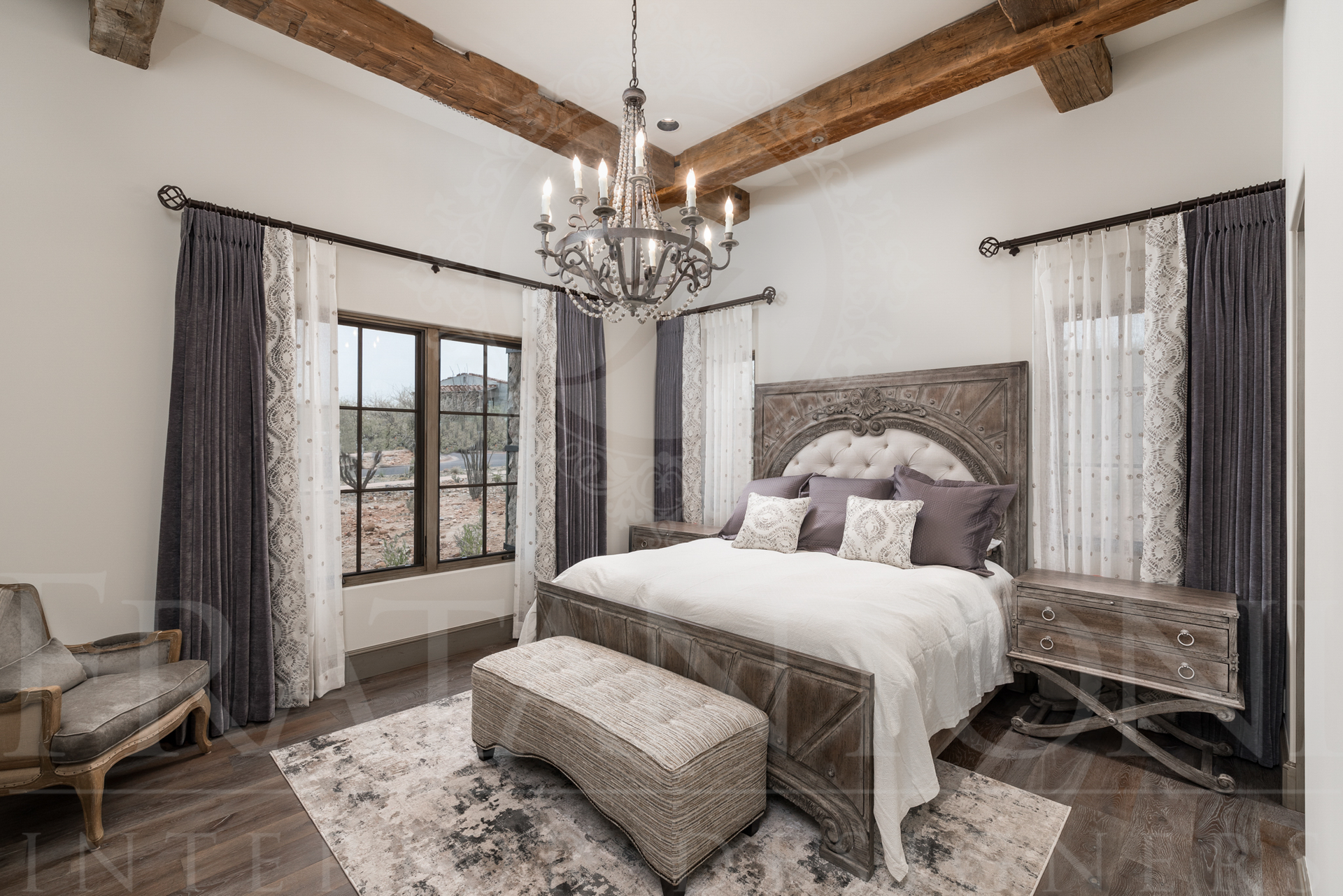 Elegant bedroom with ornate bed, chandelier, and dark curtains. Wooden beams and large window.
