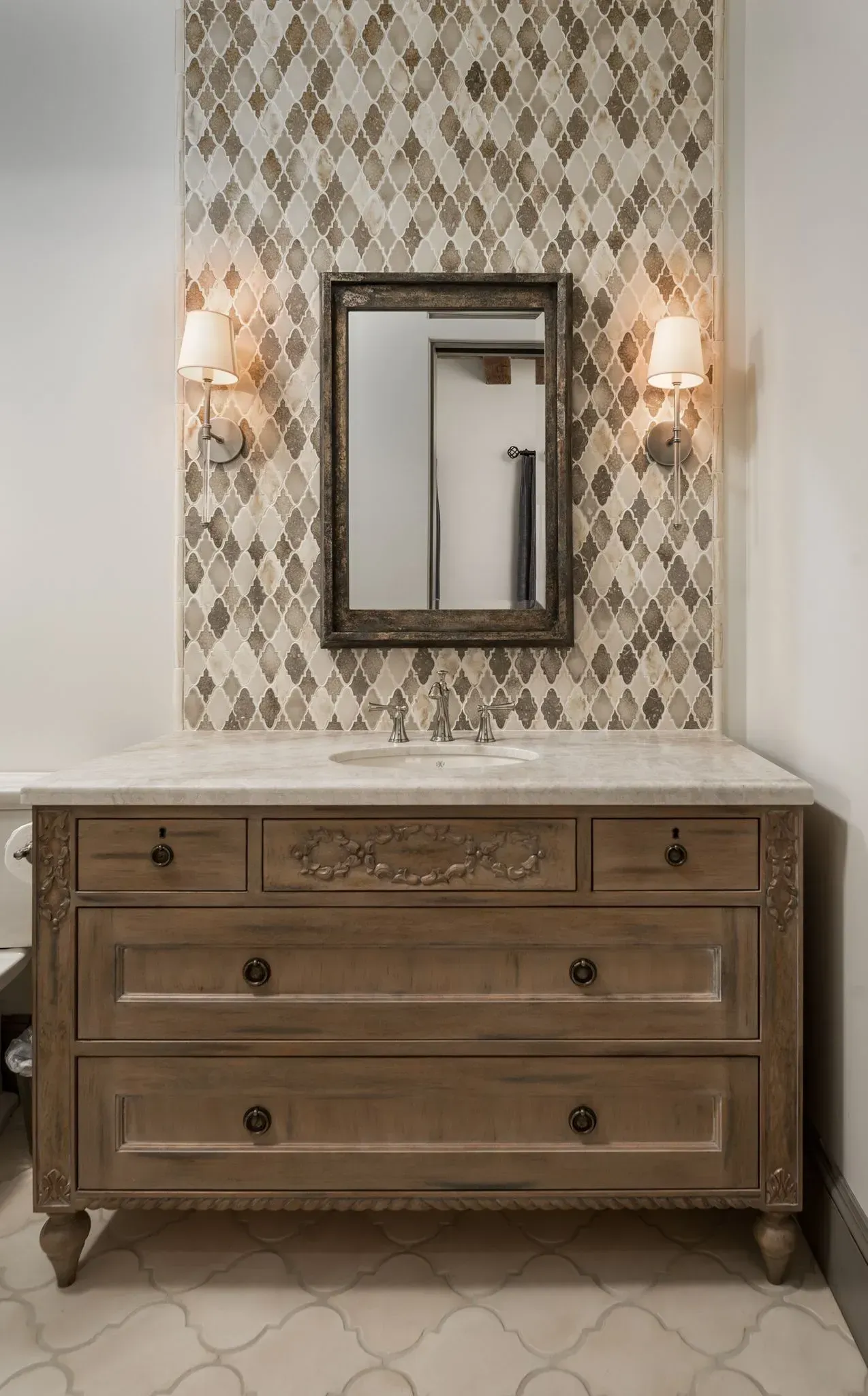 Wooden vanity with mirror and sconces, set against patterned tile backdrop.