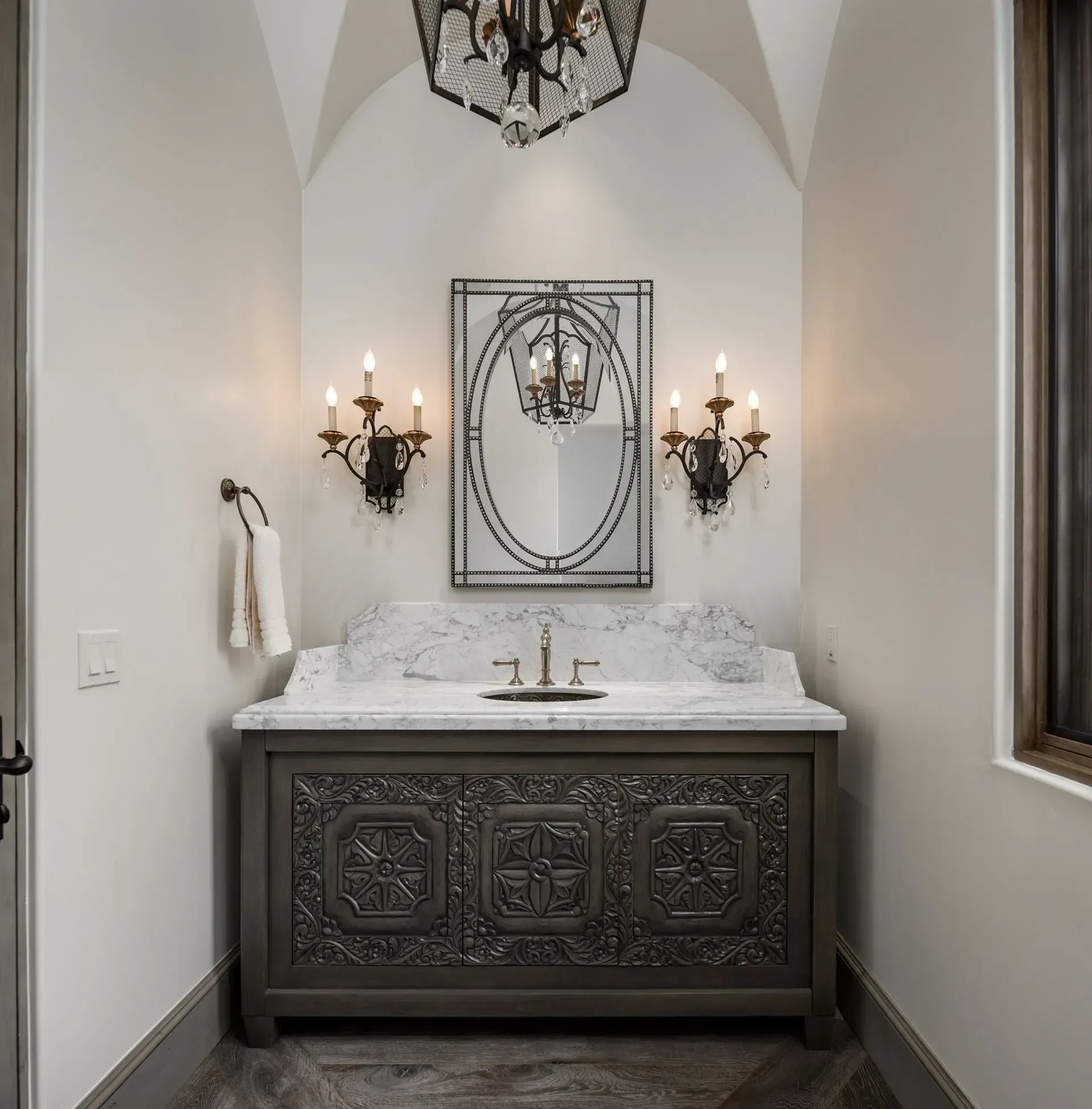 Bathroom with ornate gray vanity, marble countertop, decorative mirror, and sconces.