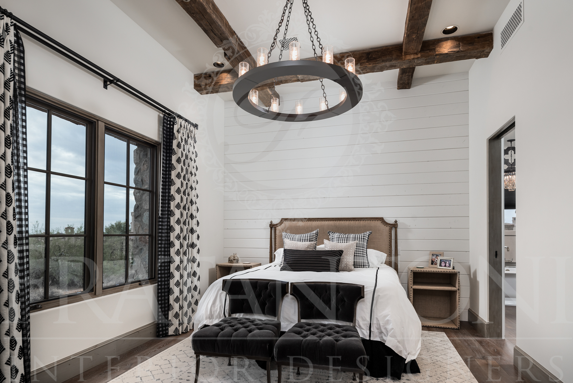 Bedroom with white walls, wood beams, a king size bed, black chairs, and a large window with patterned curtains designed by Fratantoni Interior Designers in scottsdale arizona