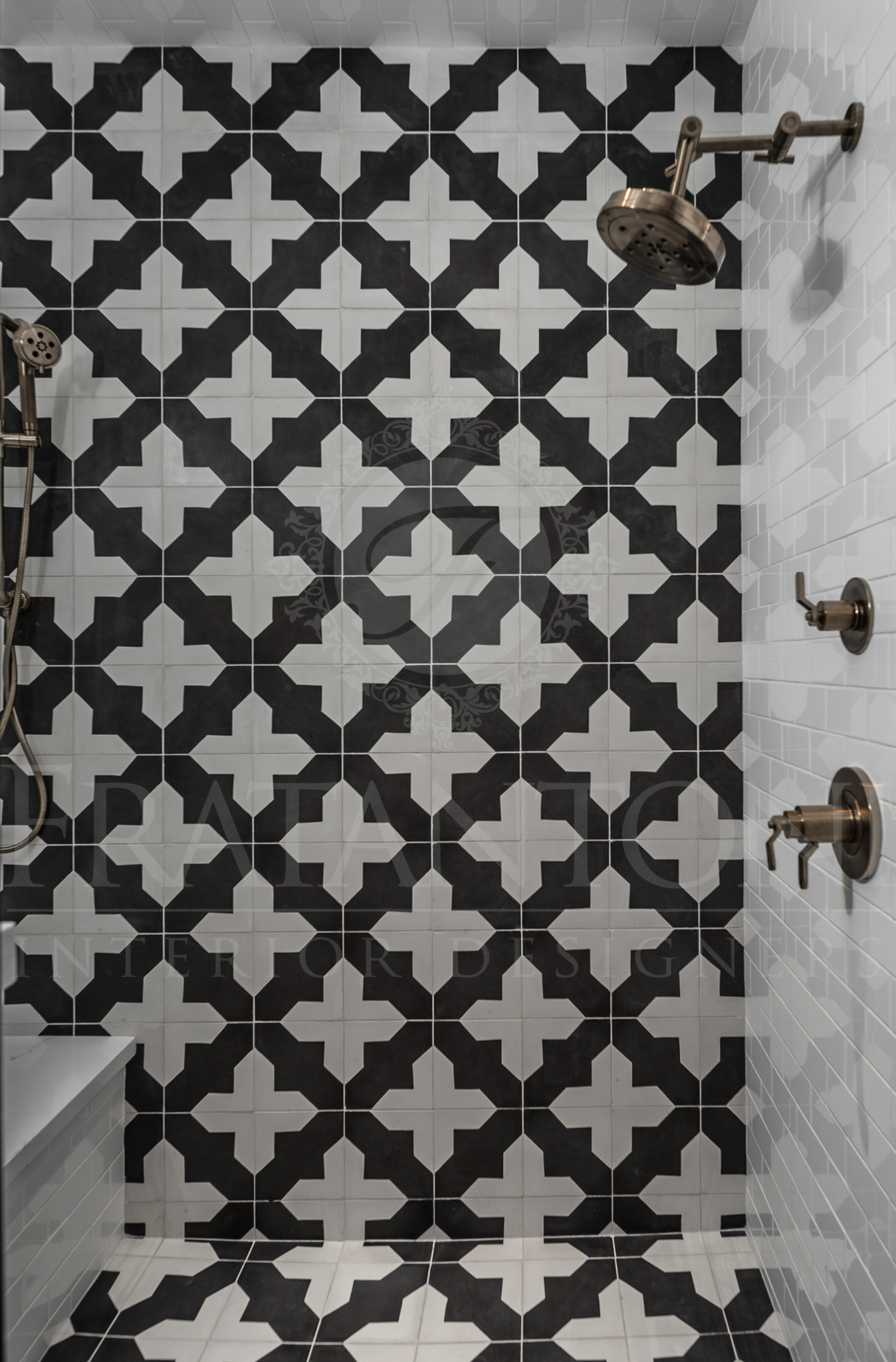 Shower with black and white patterned tile on the back wall and floor, bronze fixtures.