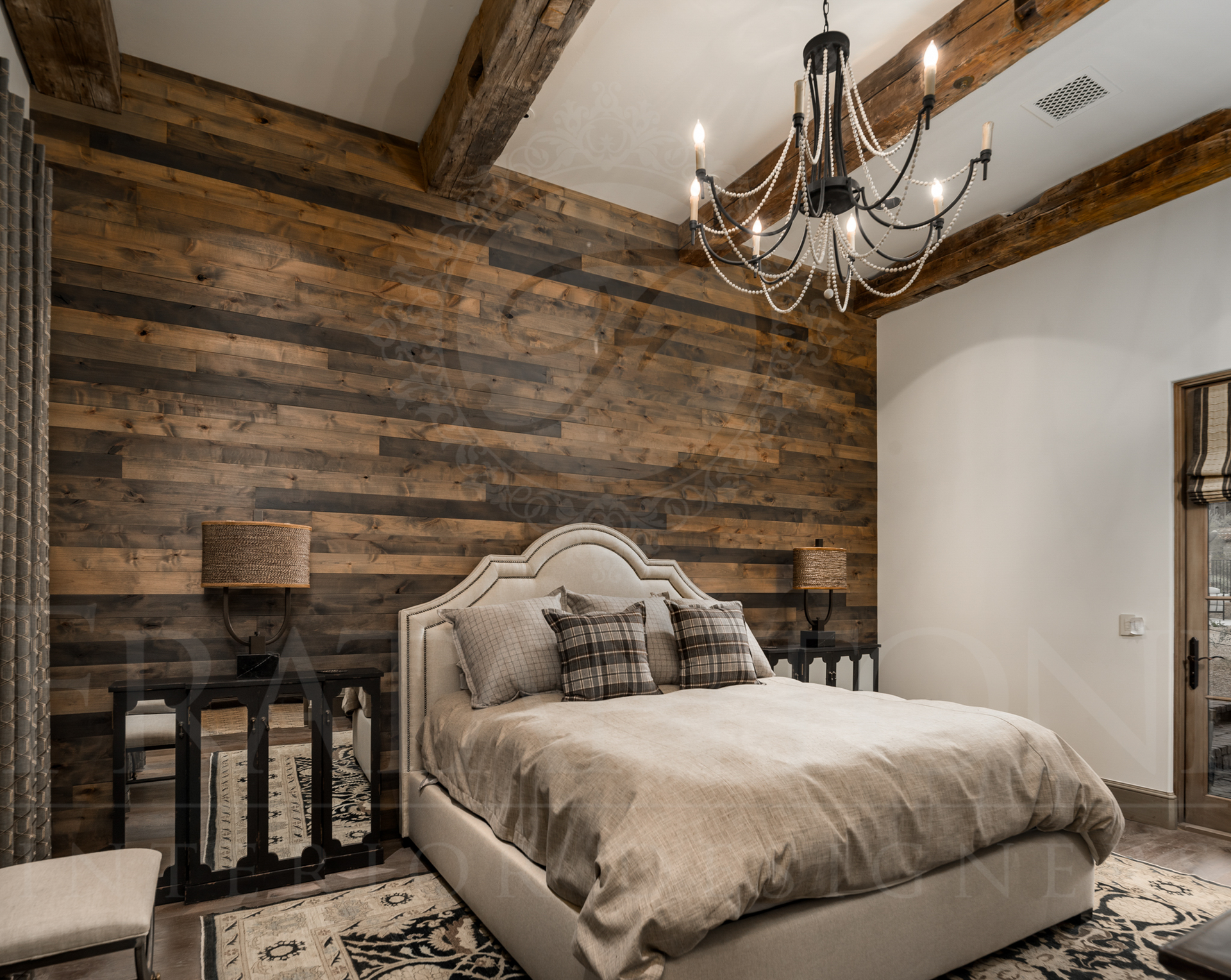 Bedroom with wood-paneled wall, rustic beams, chandelier, bed with neutral bedding, and two bedside lamps.