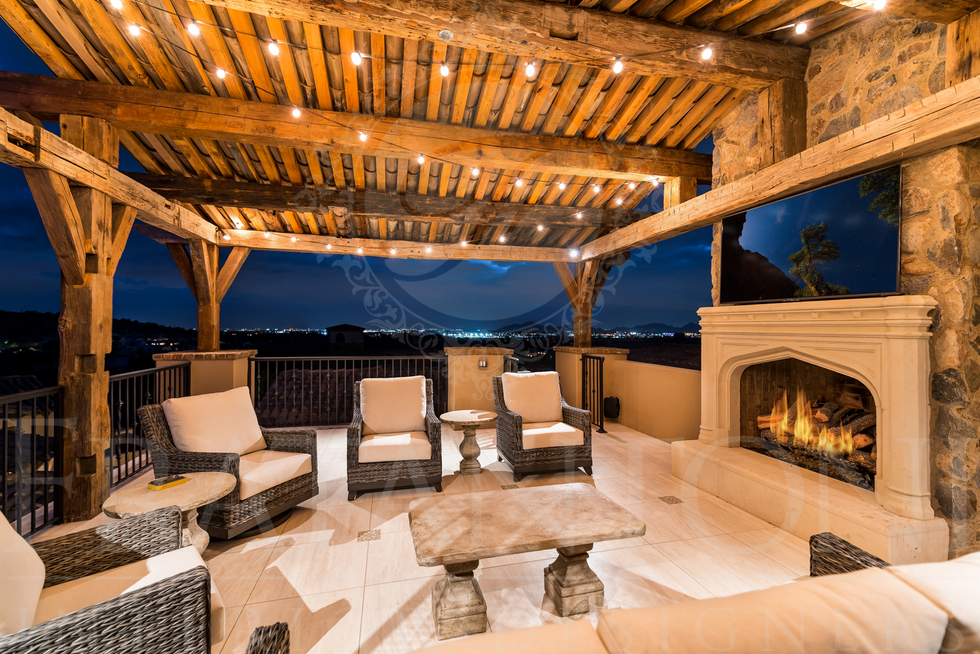 Covered patio with fireplace, seating, wooden beams, string lights, and a nighttime city view. 
