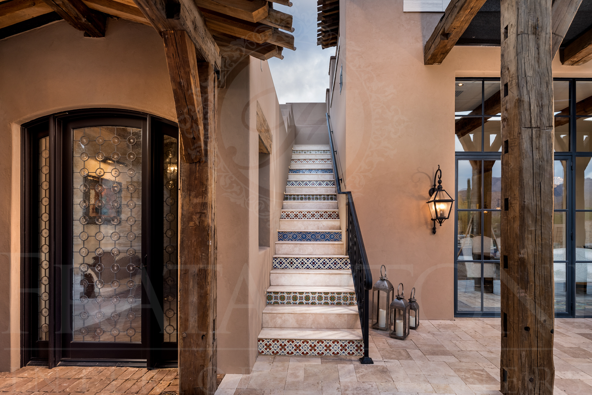 Exterior view of a home with a staircase with tile risers, stone patio, and wooden beams.