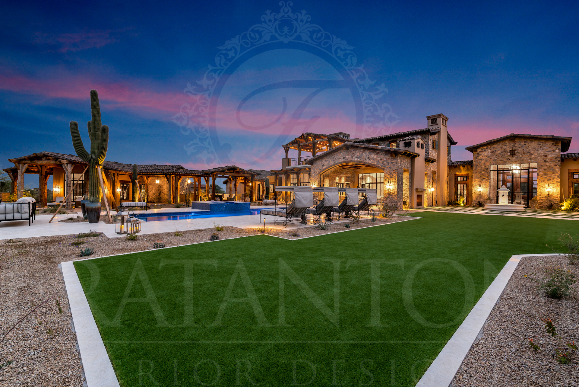 Luxurious desert estate at dusk with pool, lush lawn, and desert landscaping under a colorful sky.