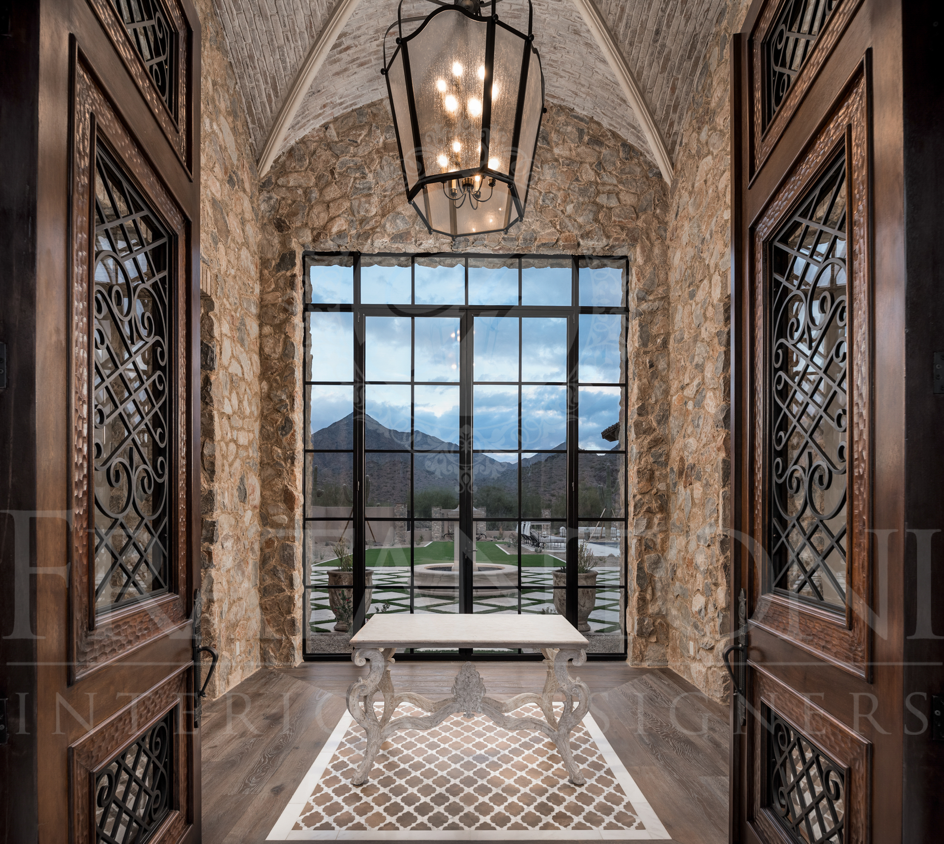 Elegant entry with large window framing mountain view, ornate doors, stone walls, vaulted stone ceiling, pendant light, and decorative floor inlay designed by Fratantoni Interior Designers in scottsdale, arizona. 