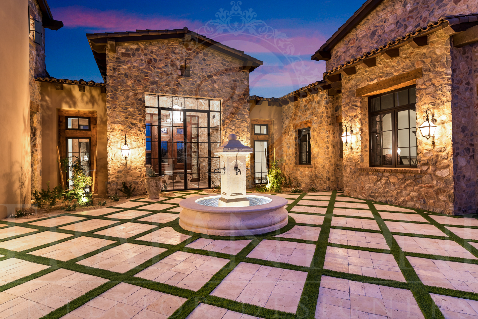 Stone courtyard with fountain and tiled flooring. Luxury home with windows surround the space designed by Fratantoni Interior Designers