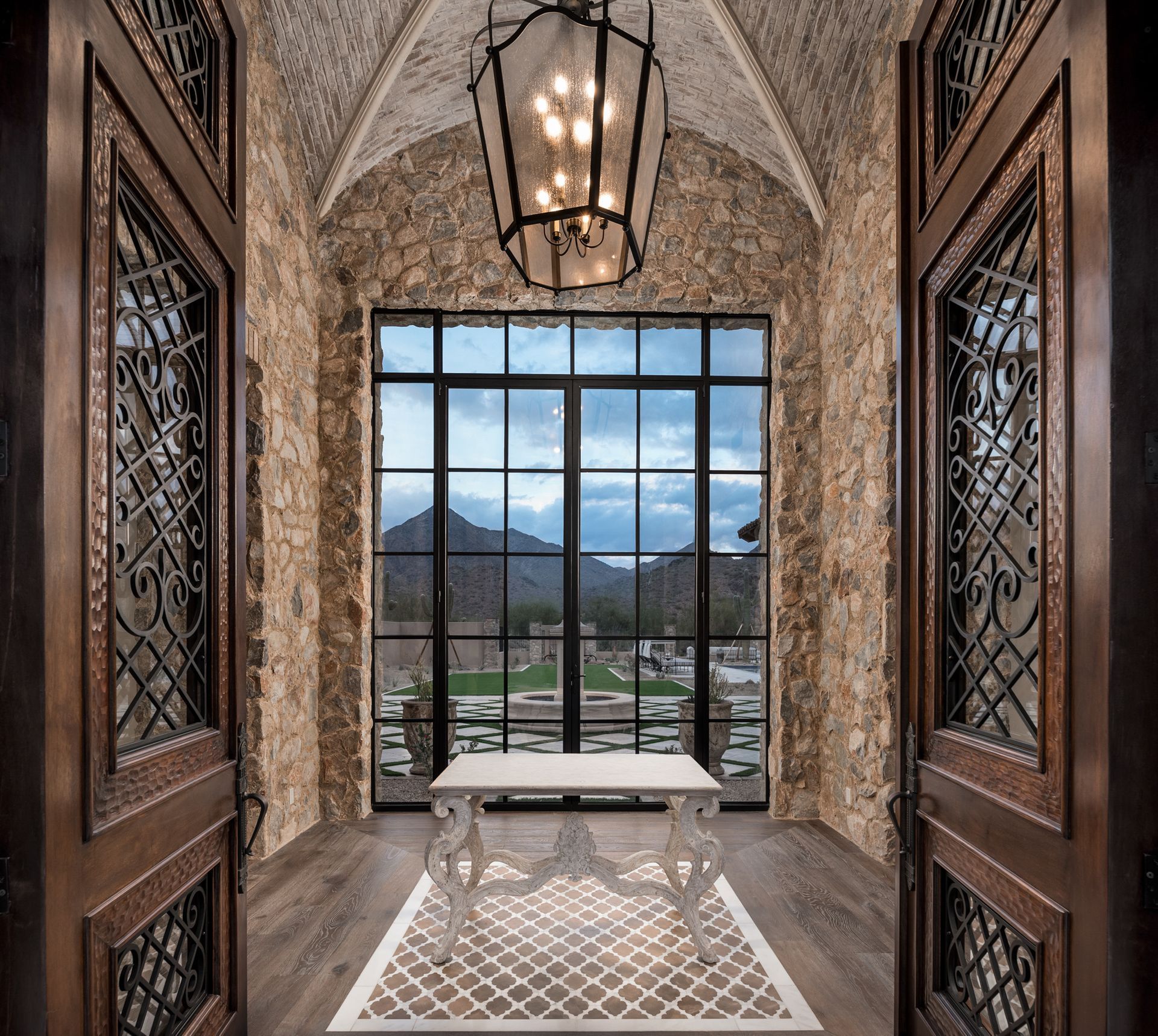 Stone hallway with carved wooden doors framing scottsdale mountain view through a large window