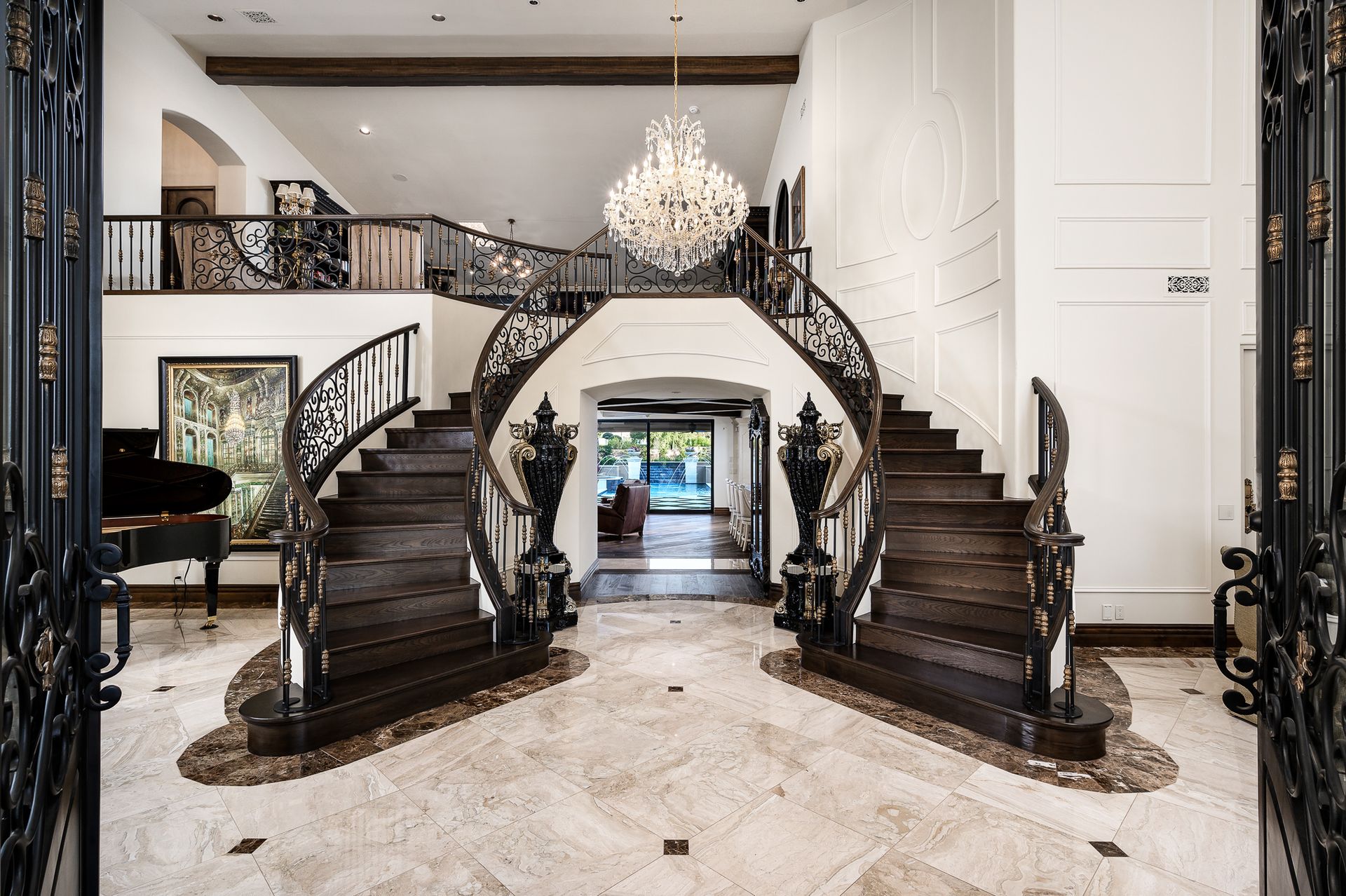 Grand curved staircase in a grand foyer with black railings, chandelier, and marble floor
