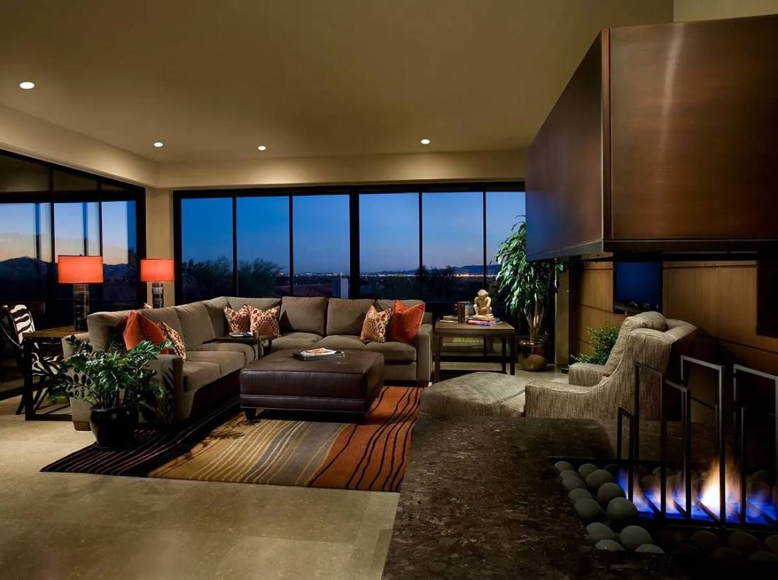 Living room at dusk with sectional sofa, fireplace, and large windows overlooking city lights.