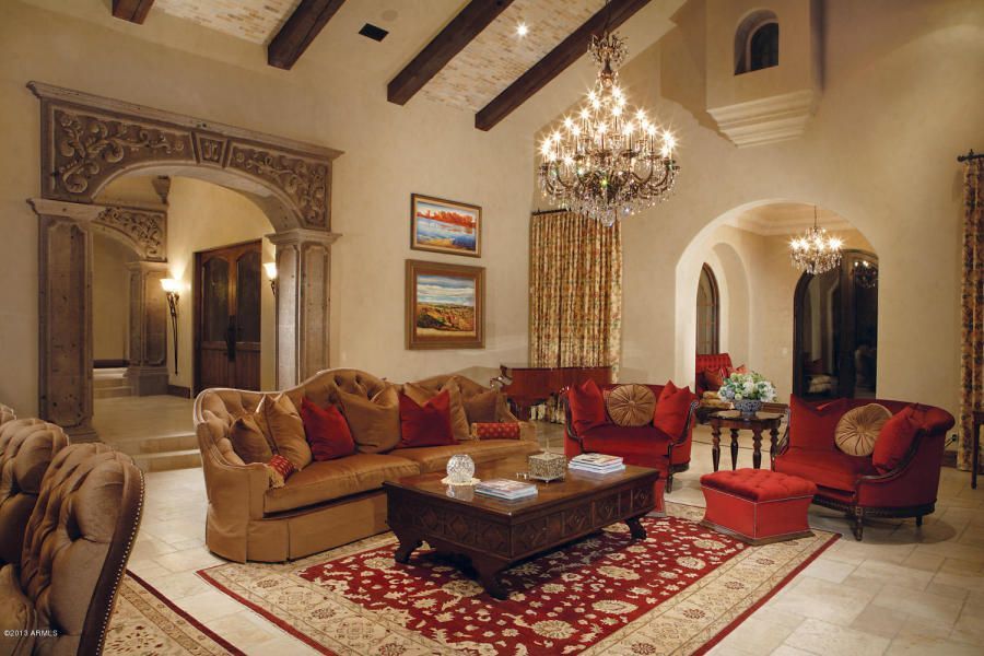 Luxurious living room with ornate details, including a chandelier, red and brown furniture, and carved archways.