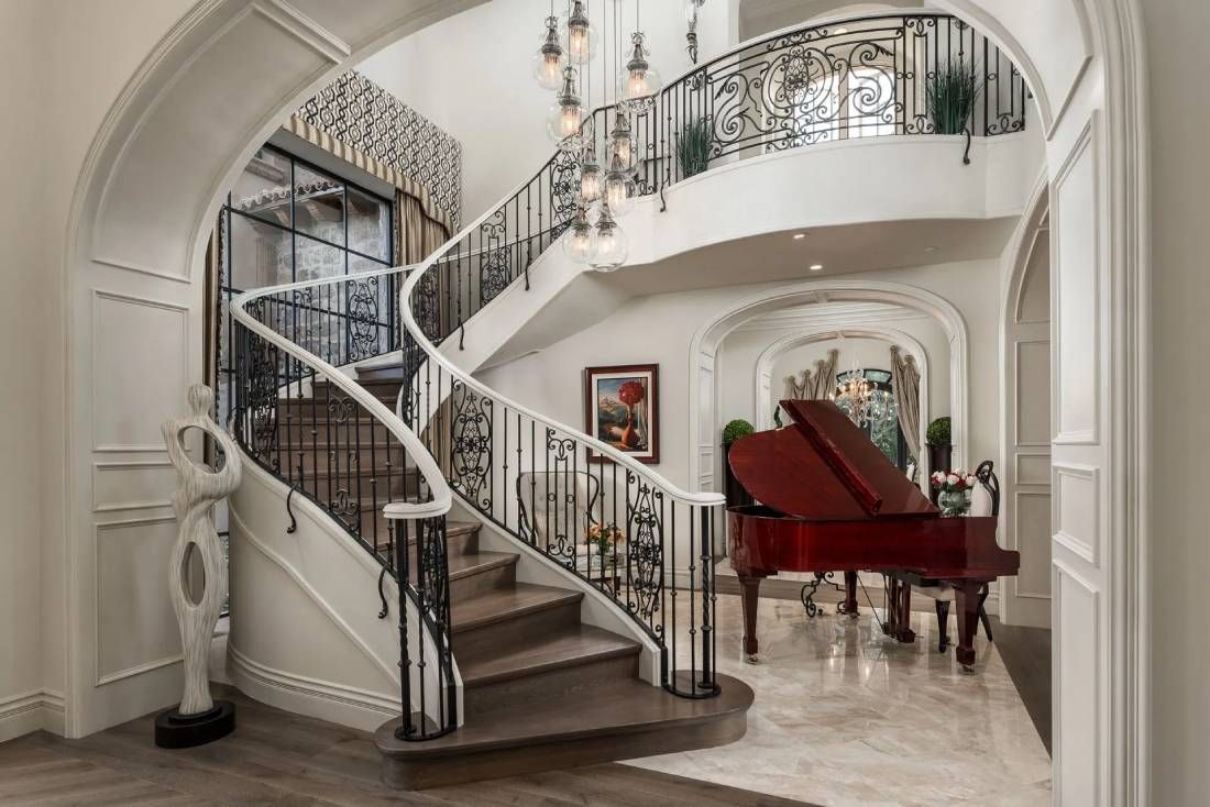 Elegant two-story foyer with winding staircase, red piano, and ornate details.