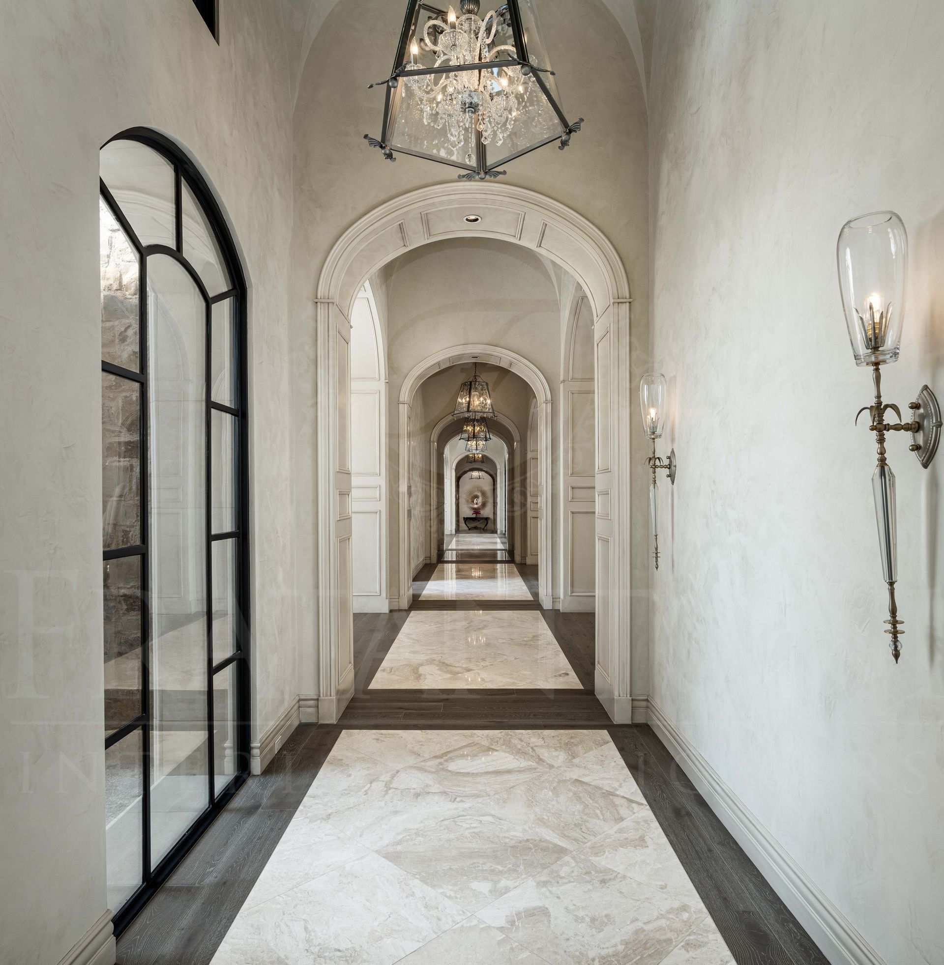 Elegant hallway with arched panel doorways, white walls, glass sconces, and patterned stone flooring in a historic interior in scottsdale, arizona