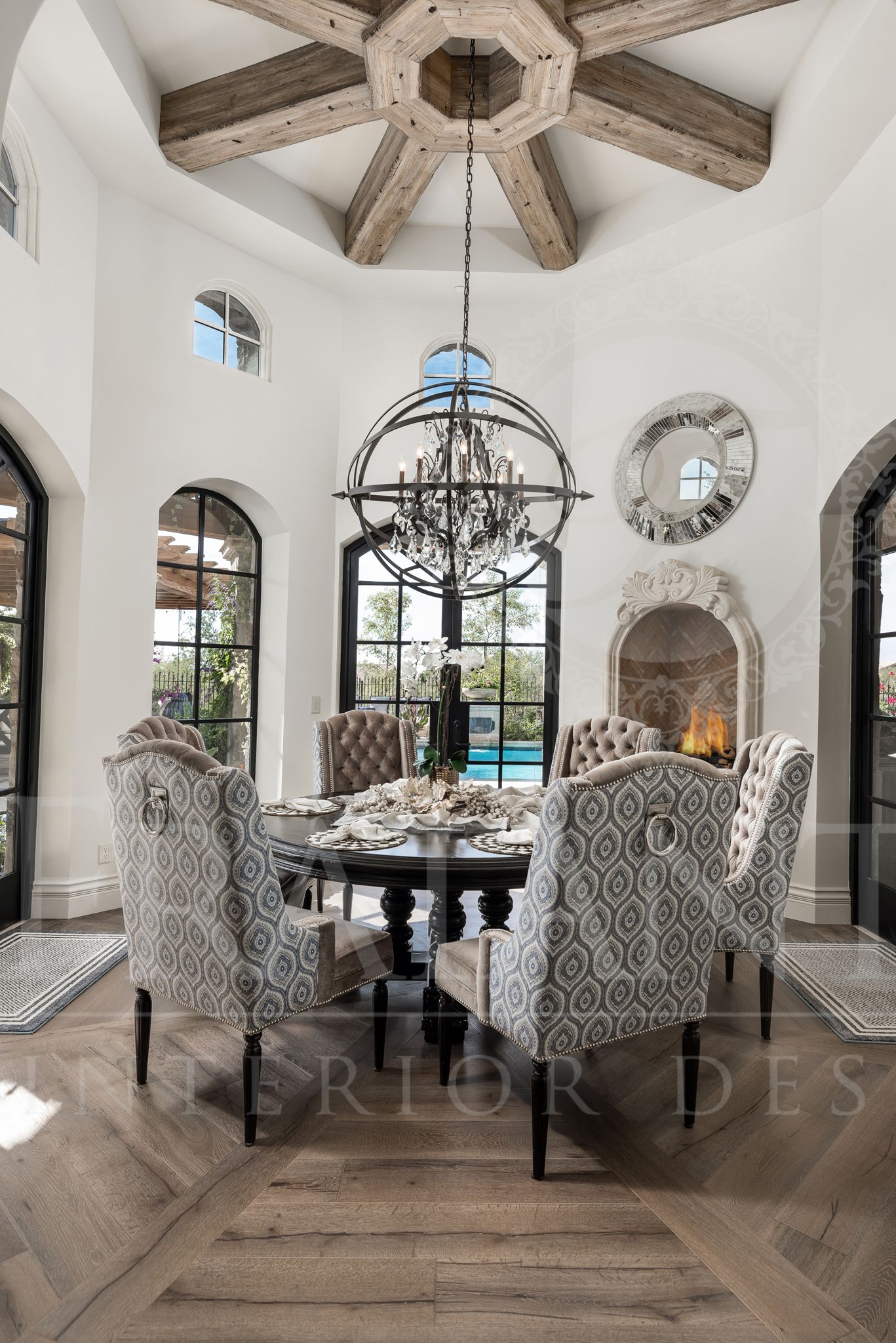 Elegant breakfast nook dining room with chandelier, round table, patterned chairs, fireplace, large windows, pool view, and wood flooring.
