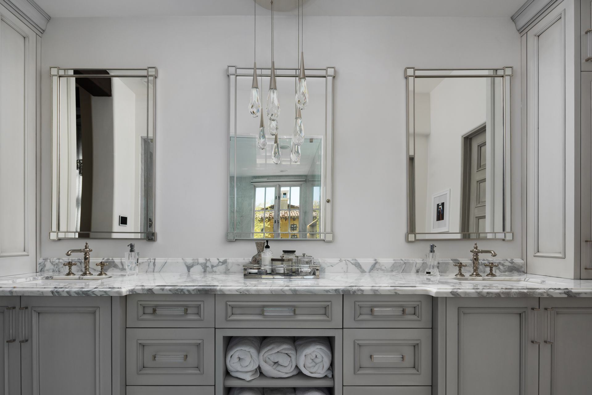 Bathroom with three mirrors above a gray vanity, marble countertop, and towel storage.