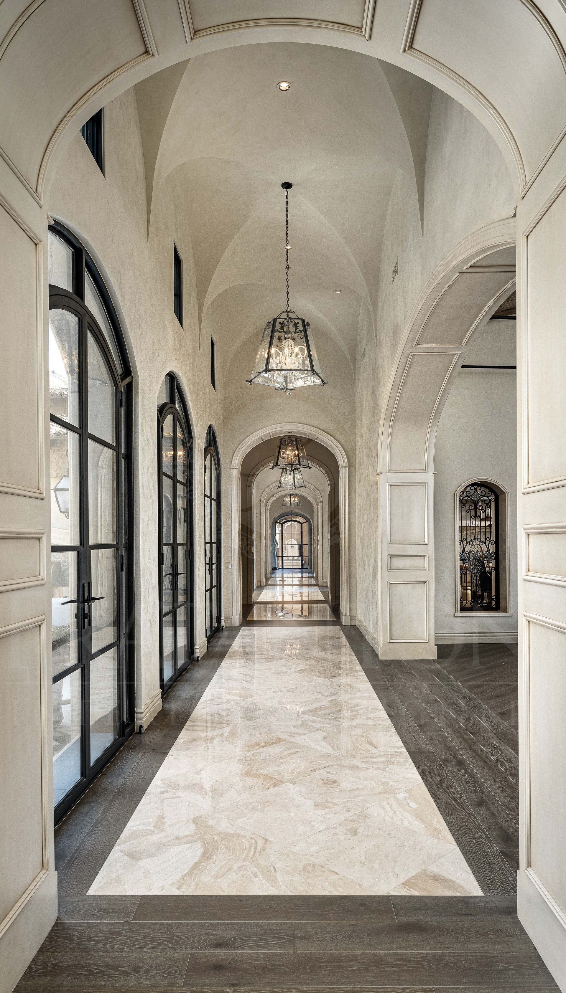 Elegant arched hallway with hanging chandeliers, tall windows, courtyard access, courtyard views, arched doorways, vaulted ceilings, and marble floors