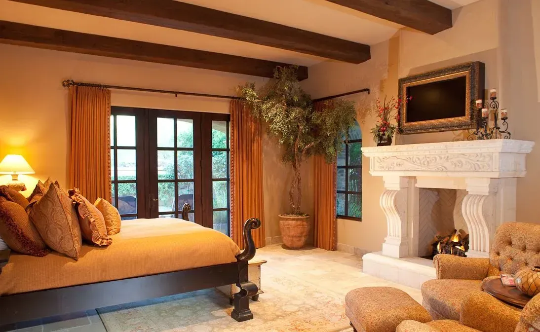 Bedroom with bed, fireplace, and French doors; warm colors, rustic decor.