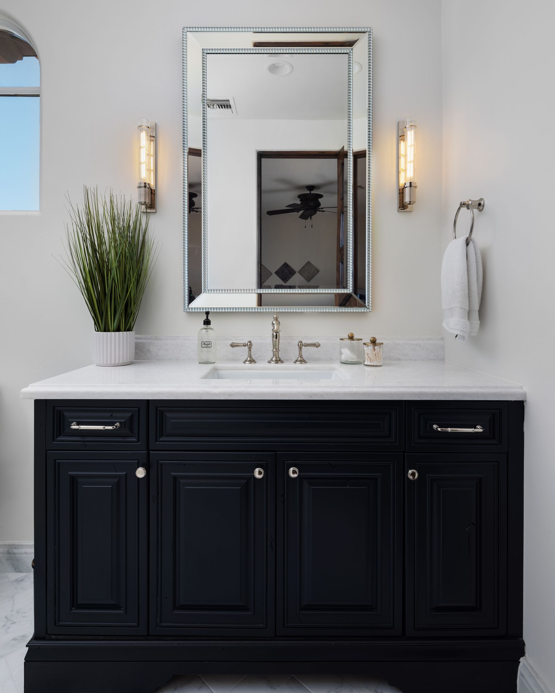 Black bathroom vanity with white countertop, mirror, and sconces.