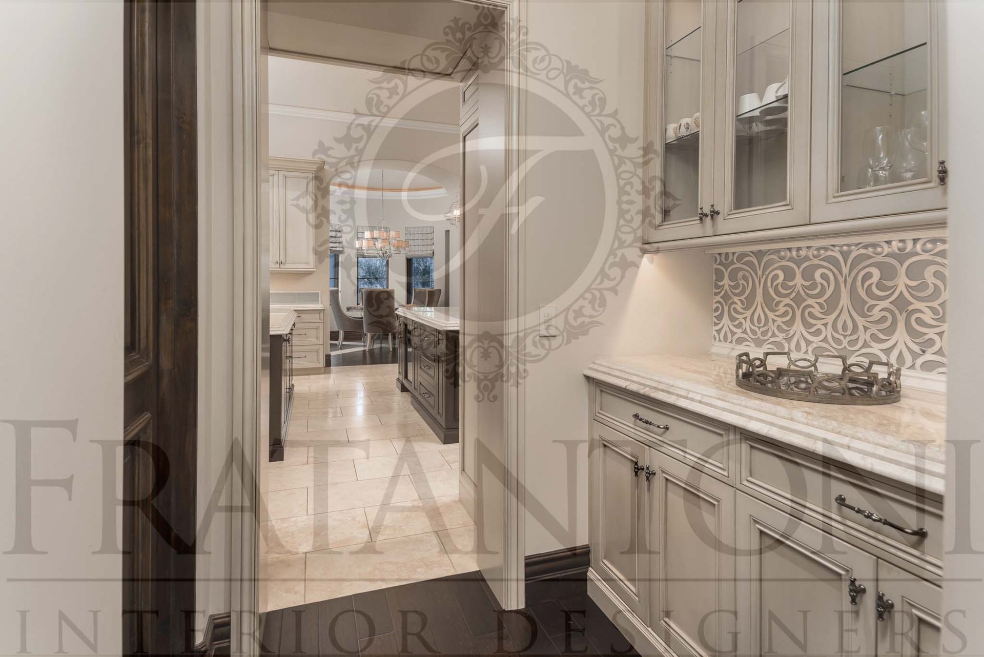 Luxurious neutral butlers pantry with beige cabinets, ornate backsplash, and a view into a kitchen beyond