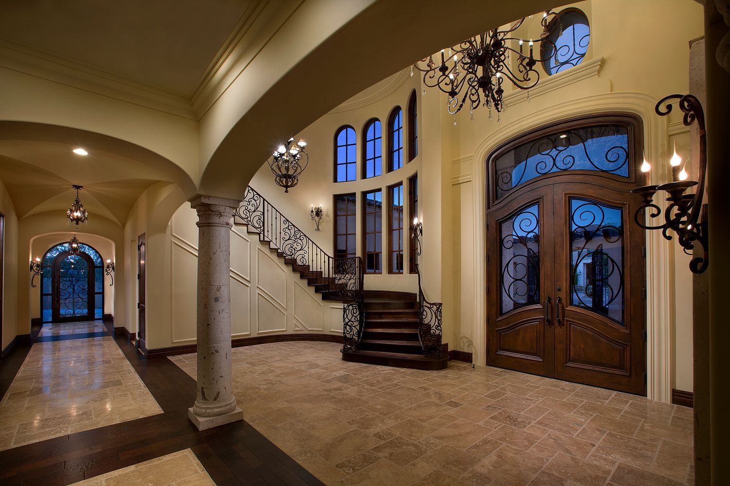 Elegant foyer with arched entryway, ornate staircase, and double wood doors.