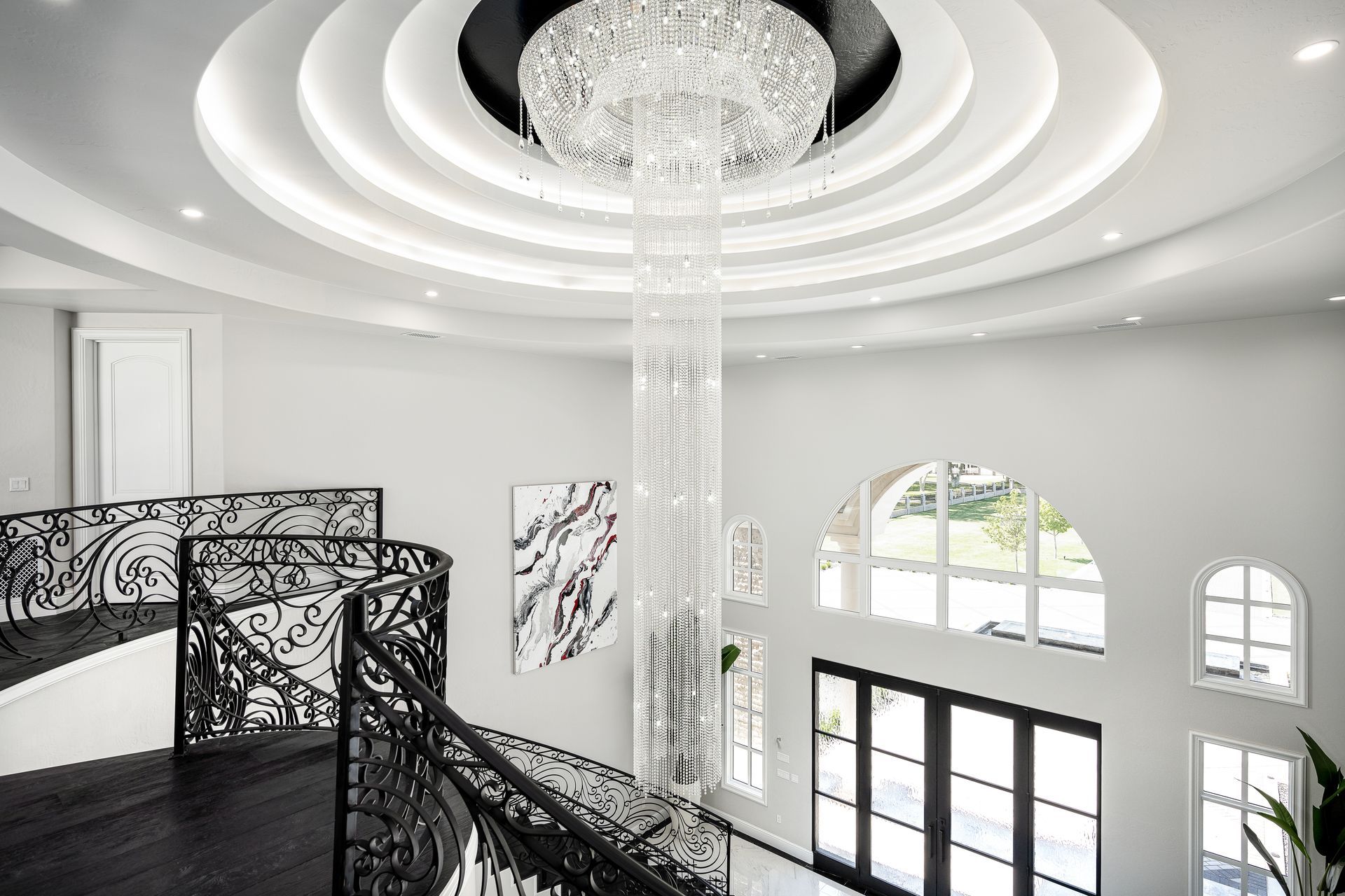 Modern home foyer with dual staircase, iron railing and a 50,000 crystal chandelier hanging from the double height ceiling