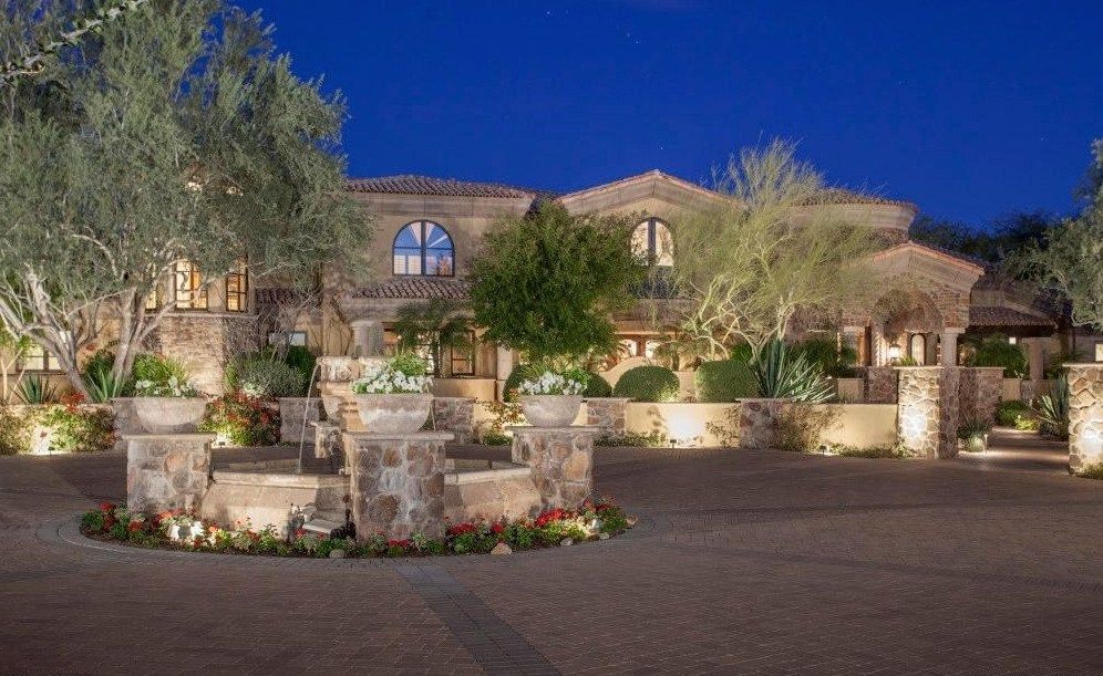 A large house with a fountain in front of it at night.