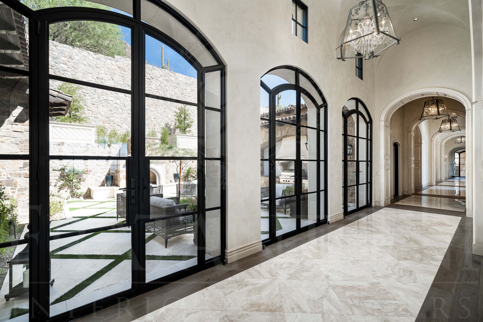 Elegant hallway with arched black-framed glass doors, courtyard views, courtyard access, marble floors, and chandelier lighting