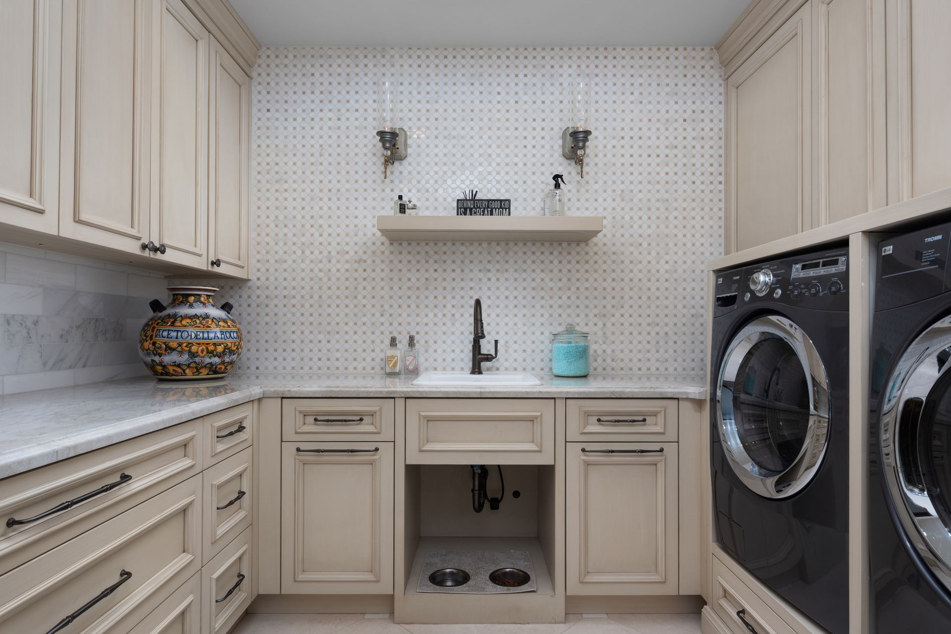 Laundry room with light cabinets, speckled backsplash, and dark washer/dryer.