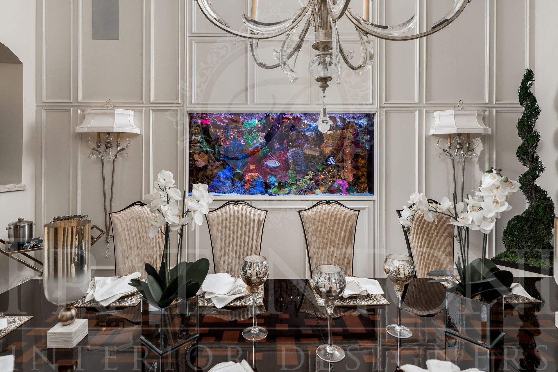 Elegant formal dining room with large aquarium built into wall, paneled walls, wall sconces, chandelier, and set table.