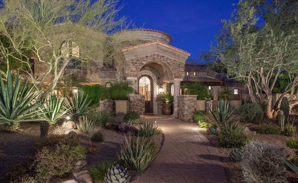 A large house with a lot of plants and trees in front of it at night.