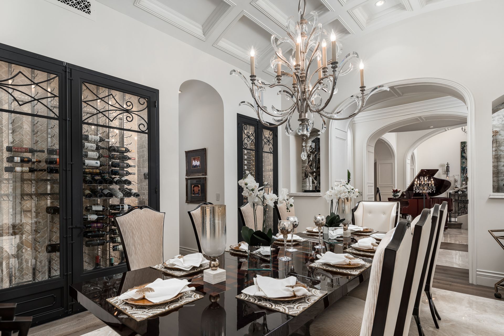 Elegant dining room with black table, chandelier, and arched doorway to a piano room.
