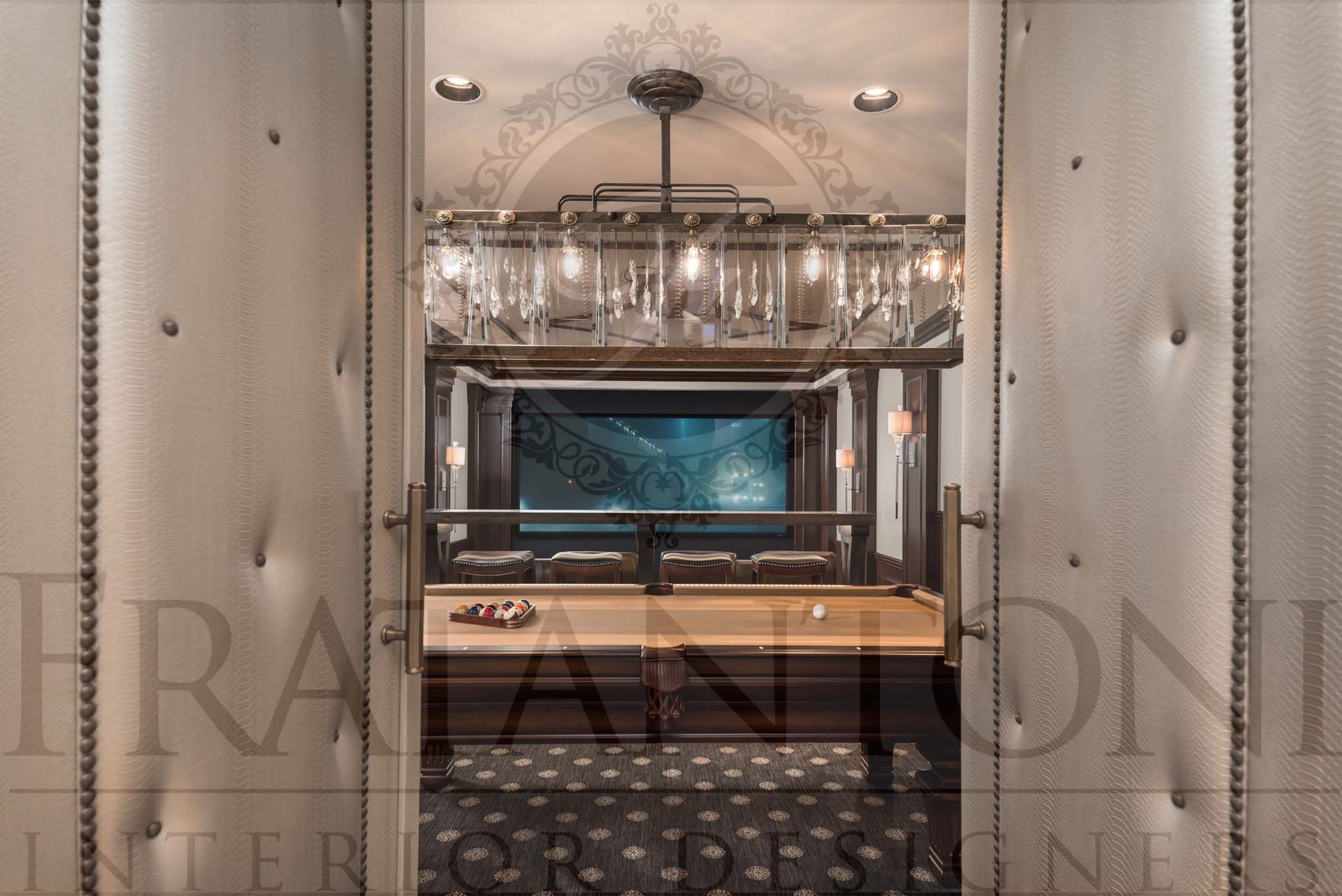 Tufted walled hallway entering a game room and movie theater room with glass lighting fixture over pool table with patterned carpet