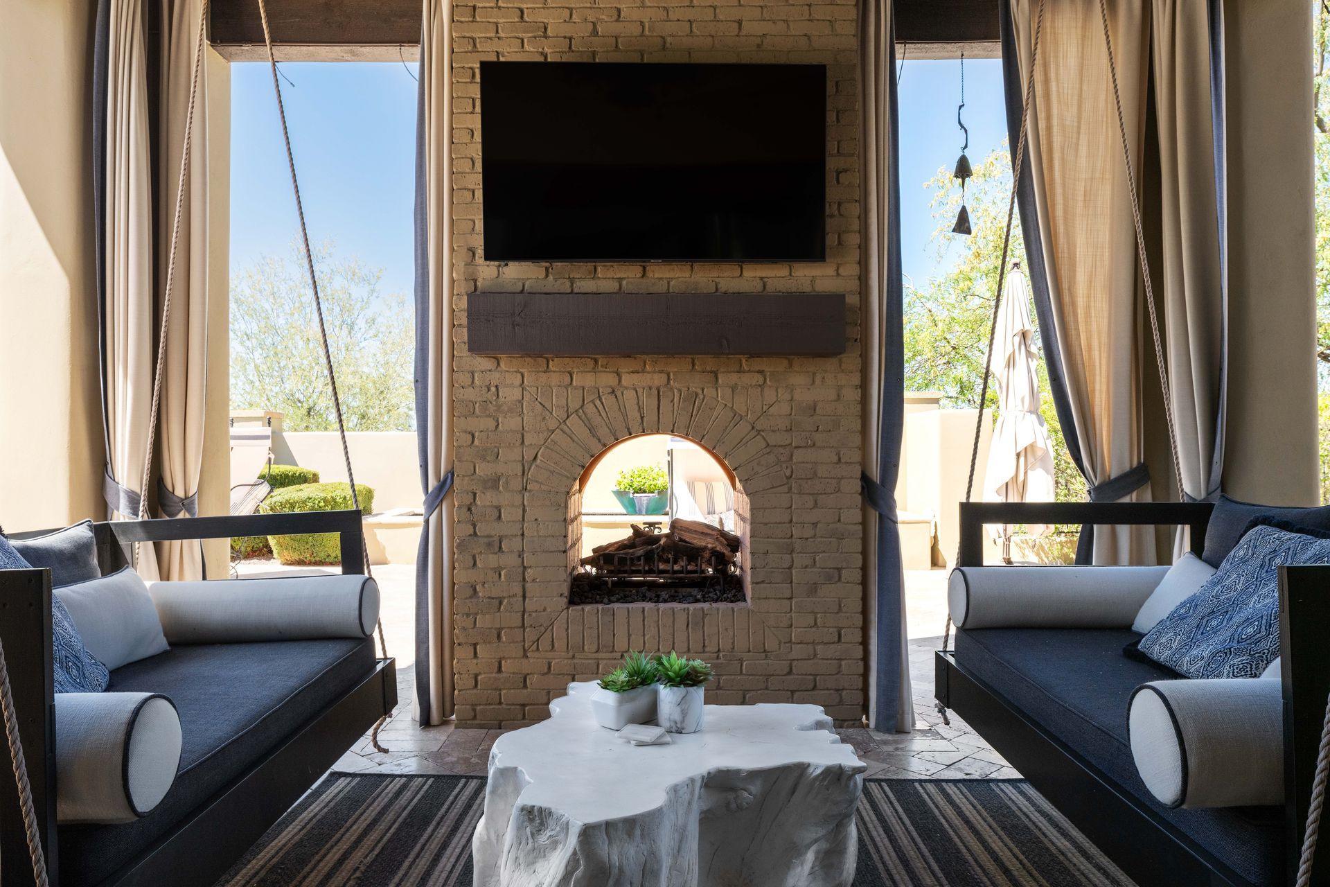 Outdoor living room with fireplace, TV, hanging sofas, and stone coffee table.