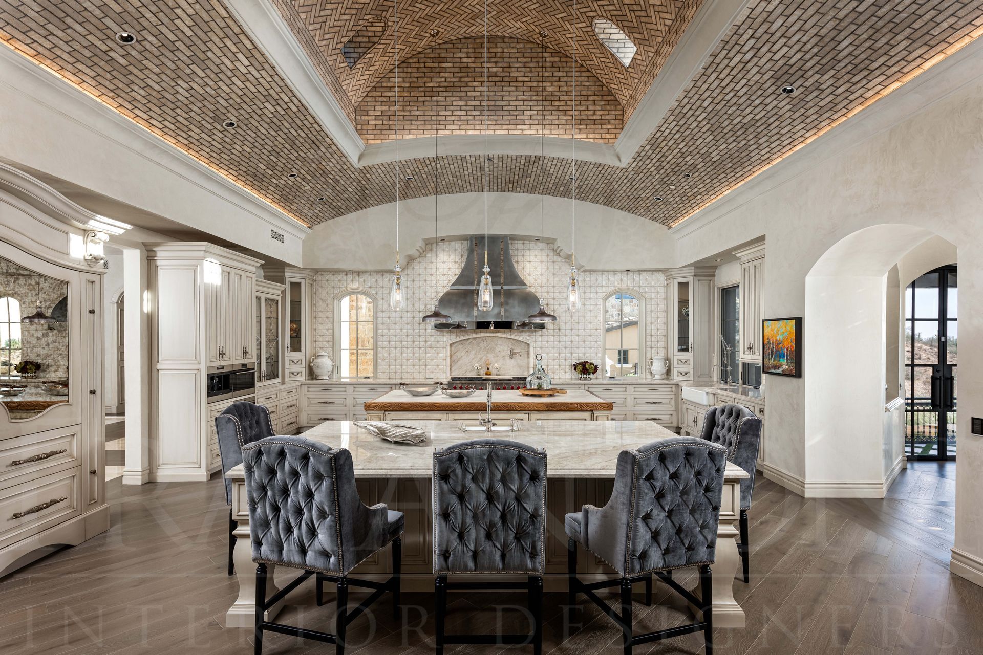 Luxury kitchen with large double islands, tufted stools, a custom stainless range hood, a vaulted brick ceiling, and arched doorways