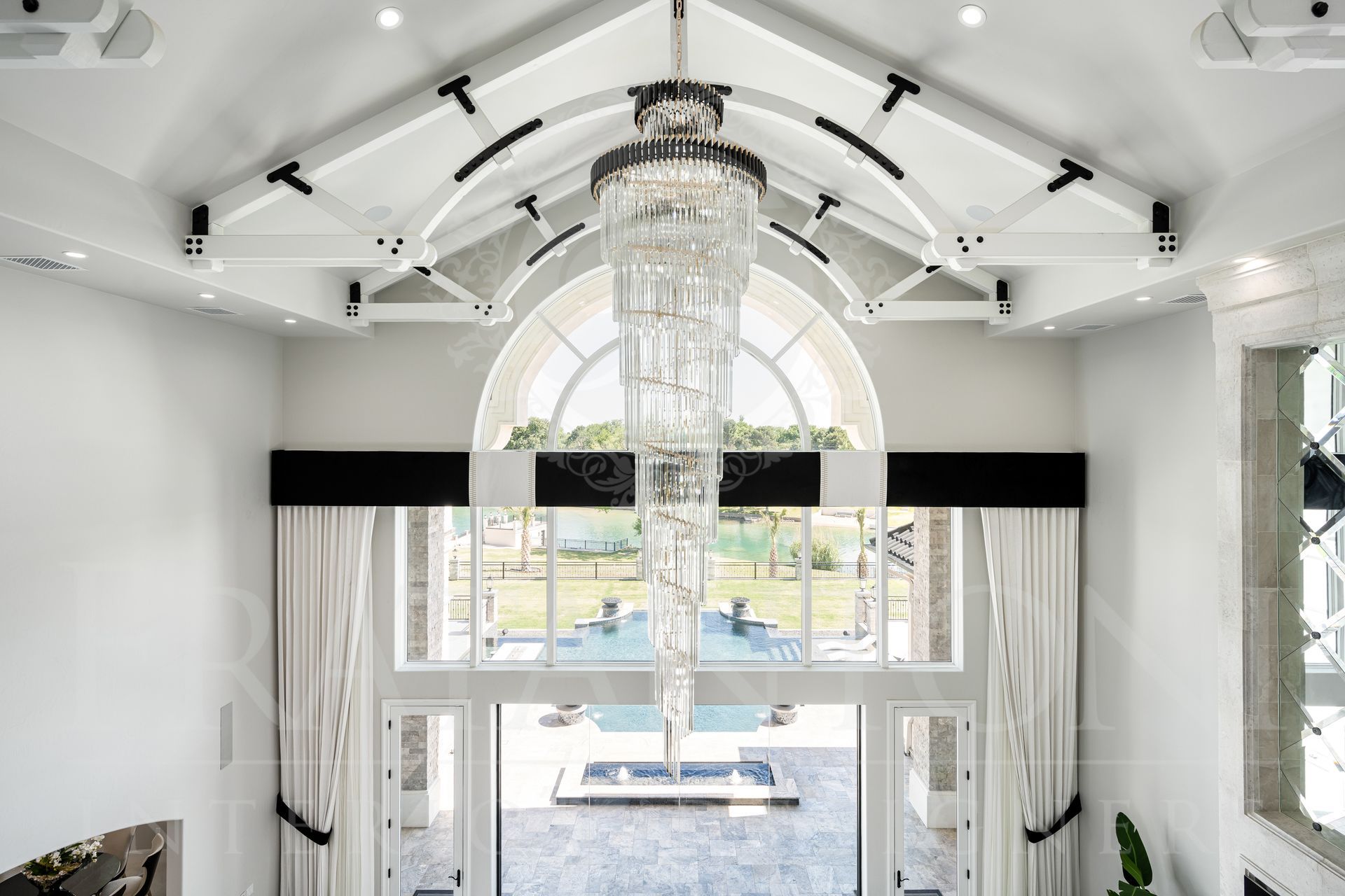 High-ceilinged grand living room with large arched window, a crystal chandelier, and white and black accents.