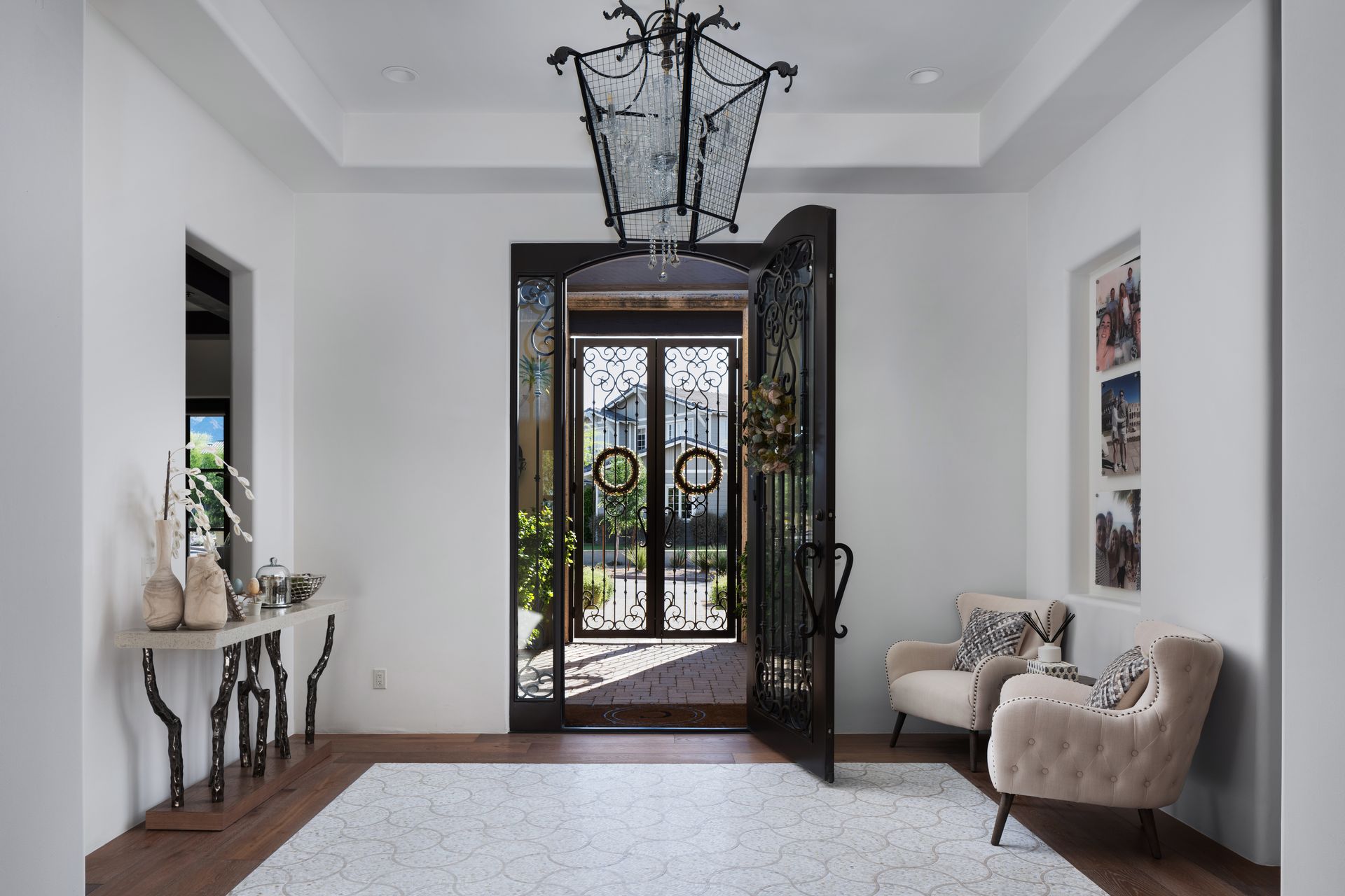Grand entryway with ornate ironwork double doors, chandelier, rug, console table, and armchair.