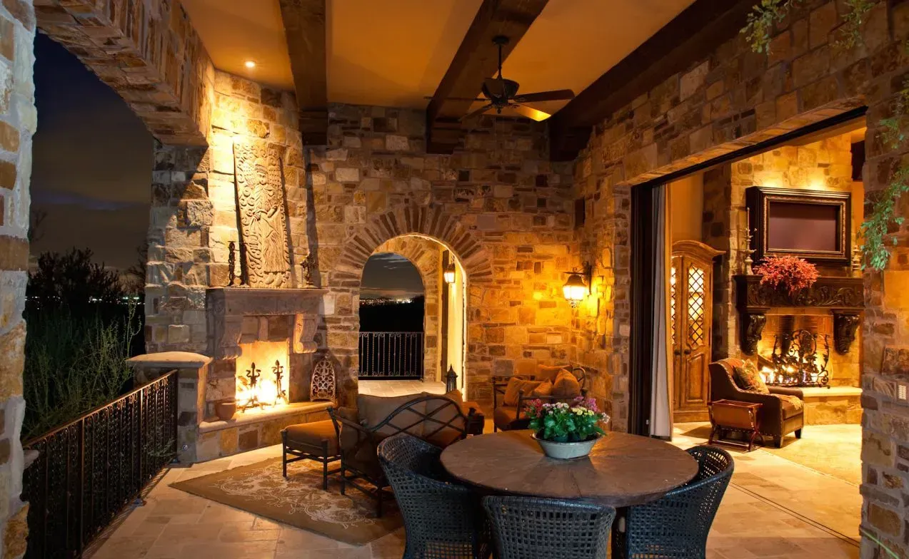 Stone patio with fireplace, arched doorways, wicker furniture, and warm lighting.