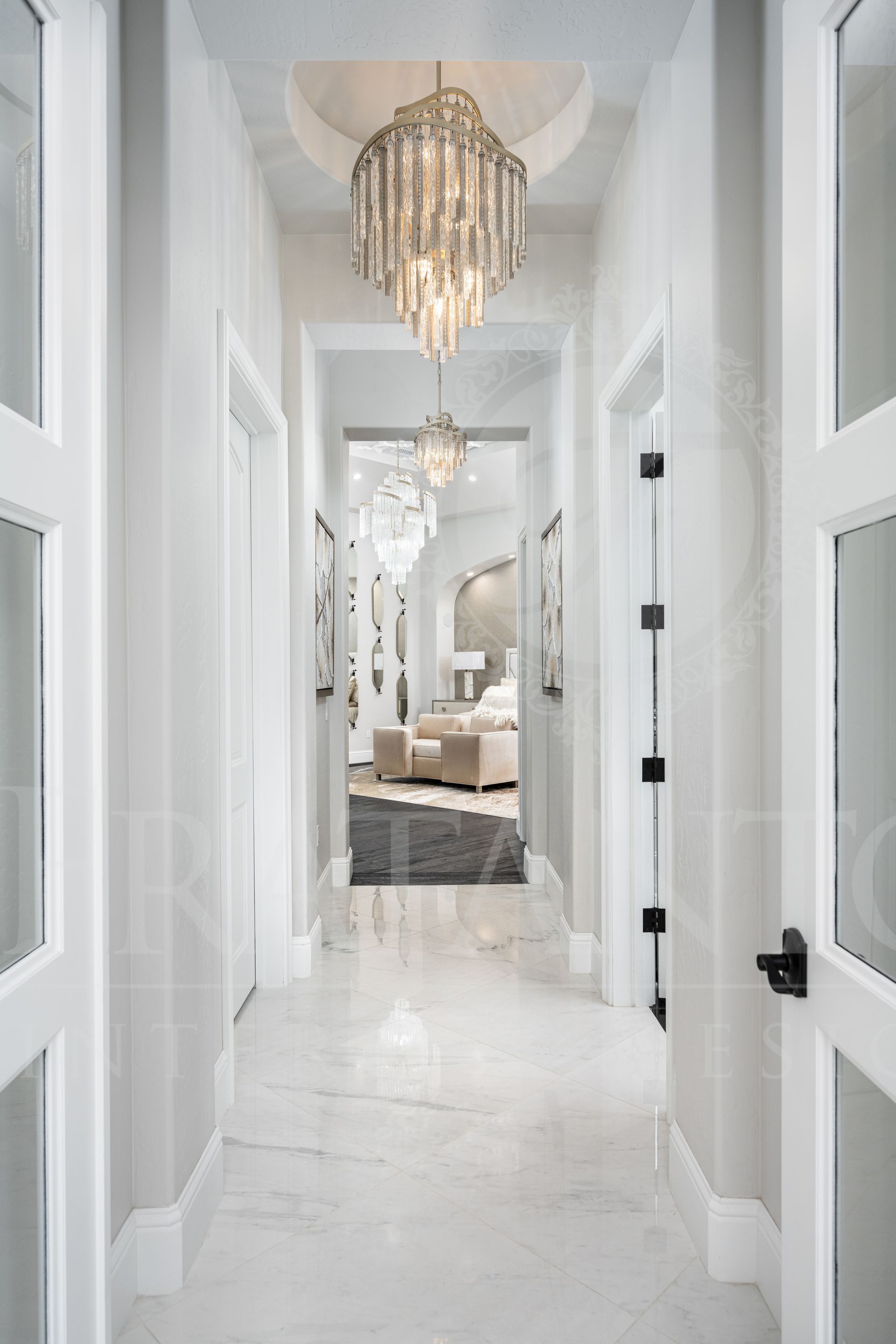Long hallway with chandeliers, marble floor, and white walls leading to a bedroom.