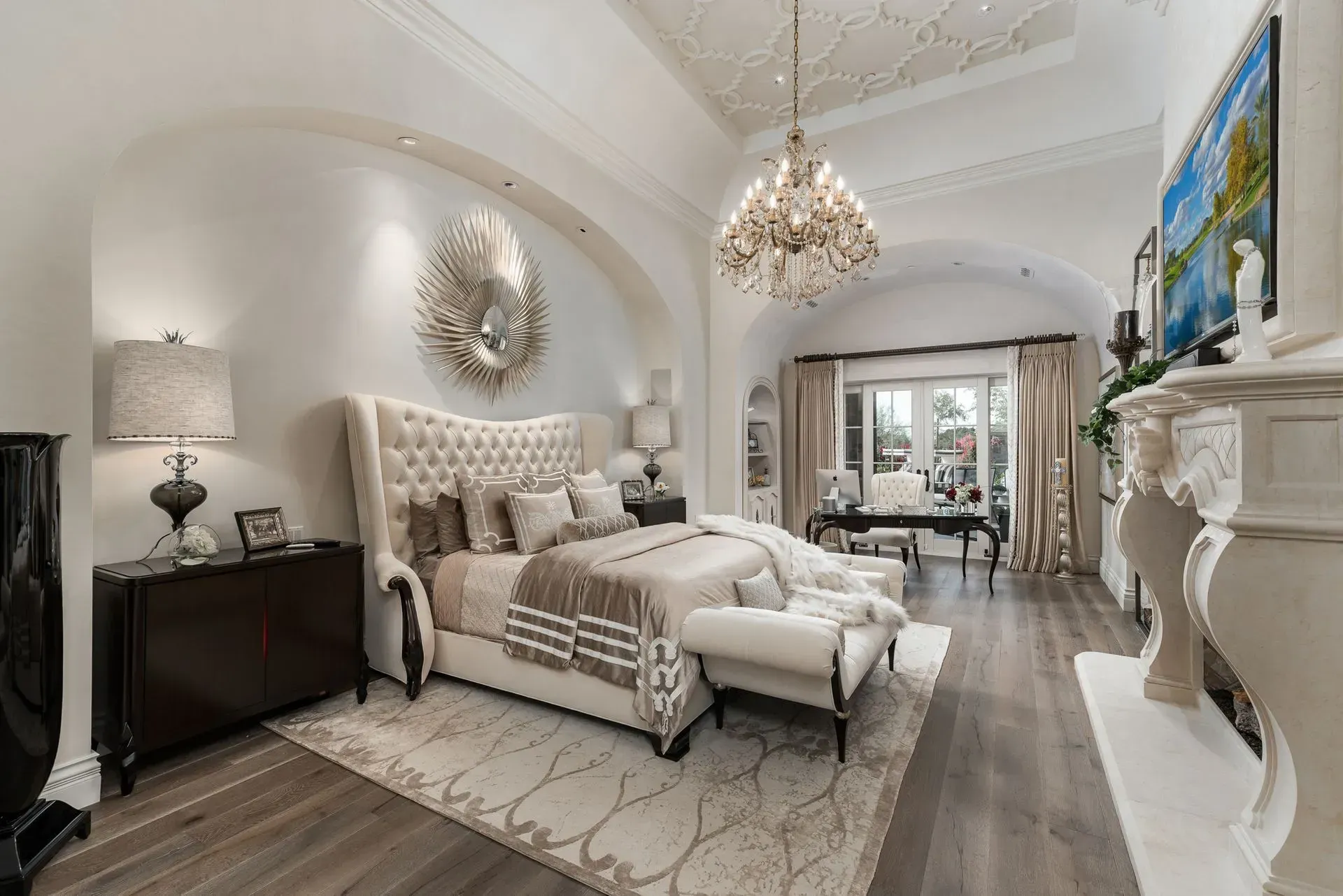 Elegant bedroom with a large bed, chandelier, fireplace, and arched doorway.