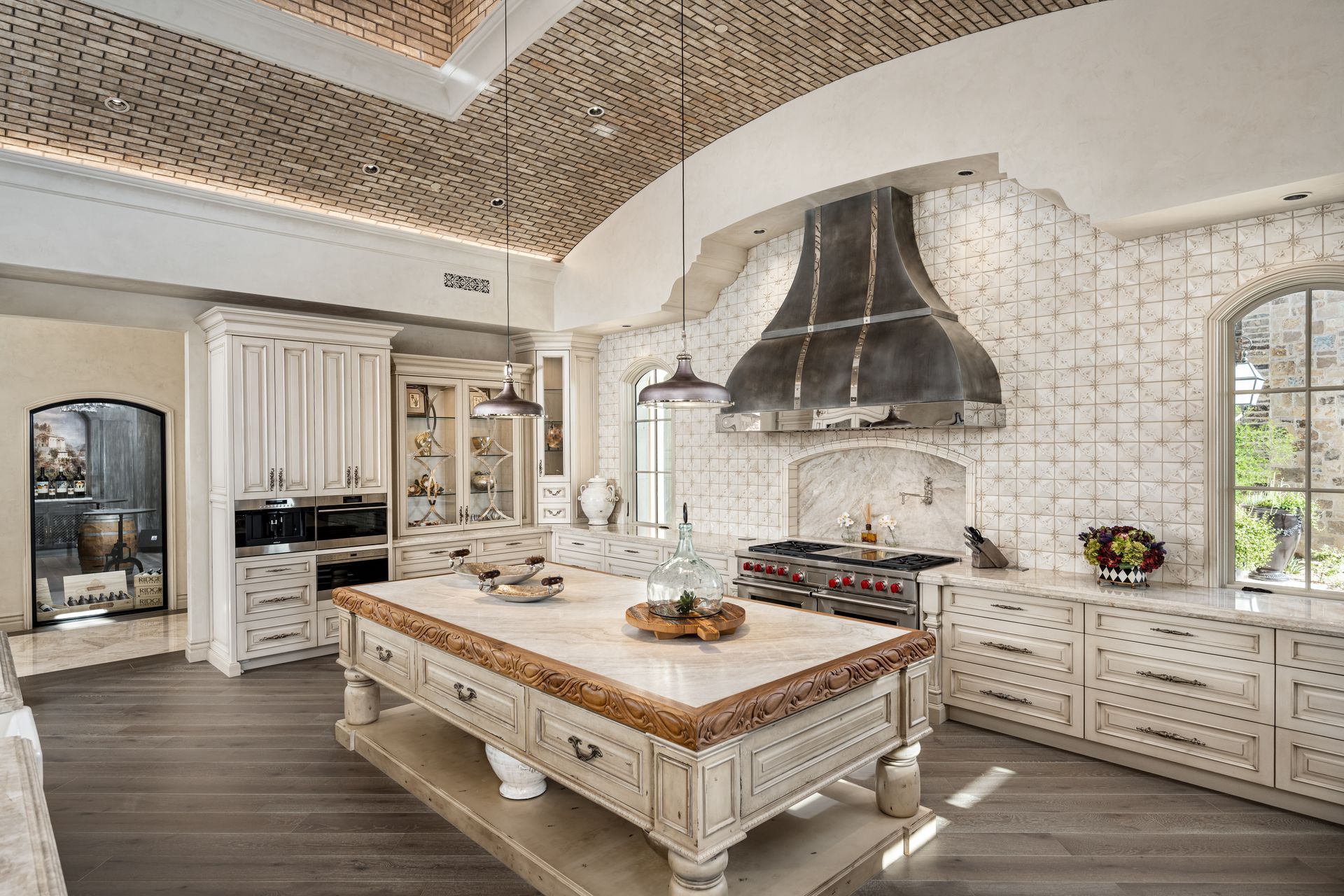 Bright, ornate kitchen with white cabinetry, large island, arched ceiling, and stainless range hood